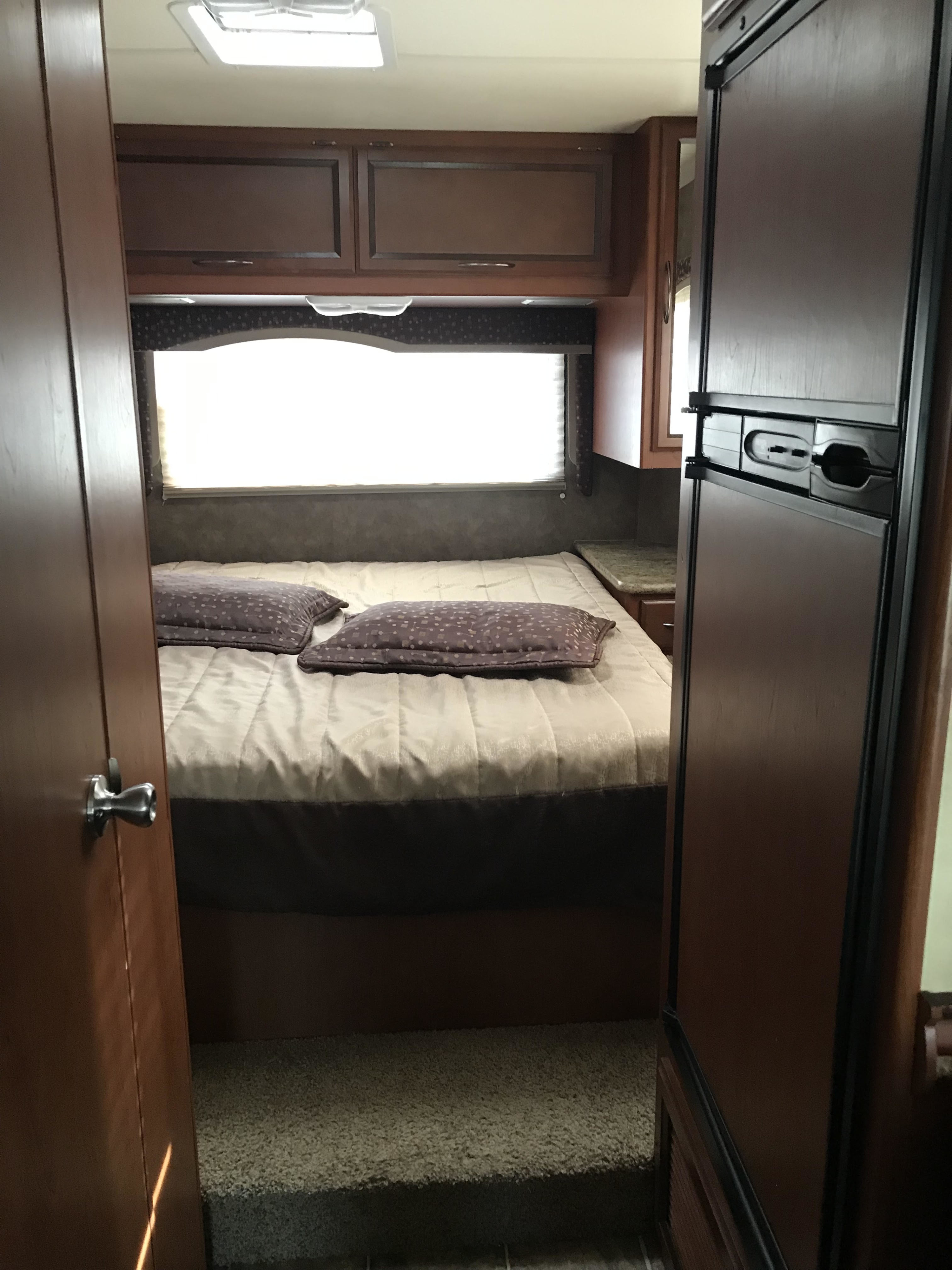 RV rental bedroom interior featuring a bed, window, and overhead cabinets, seen from a doorway next to a refrigerator.. Thor Freedom Elite 2013