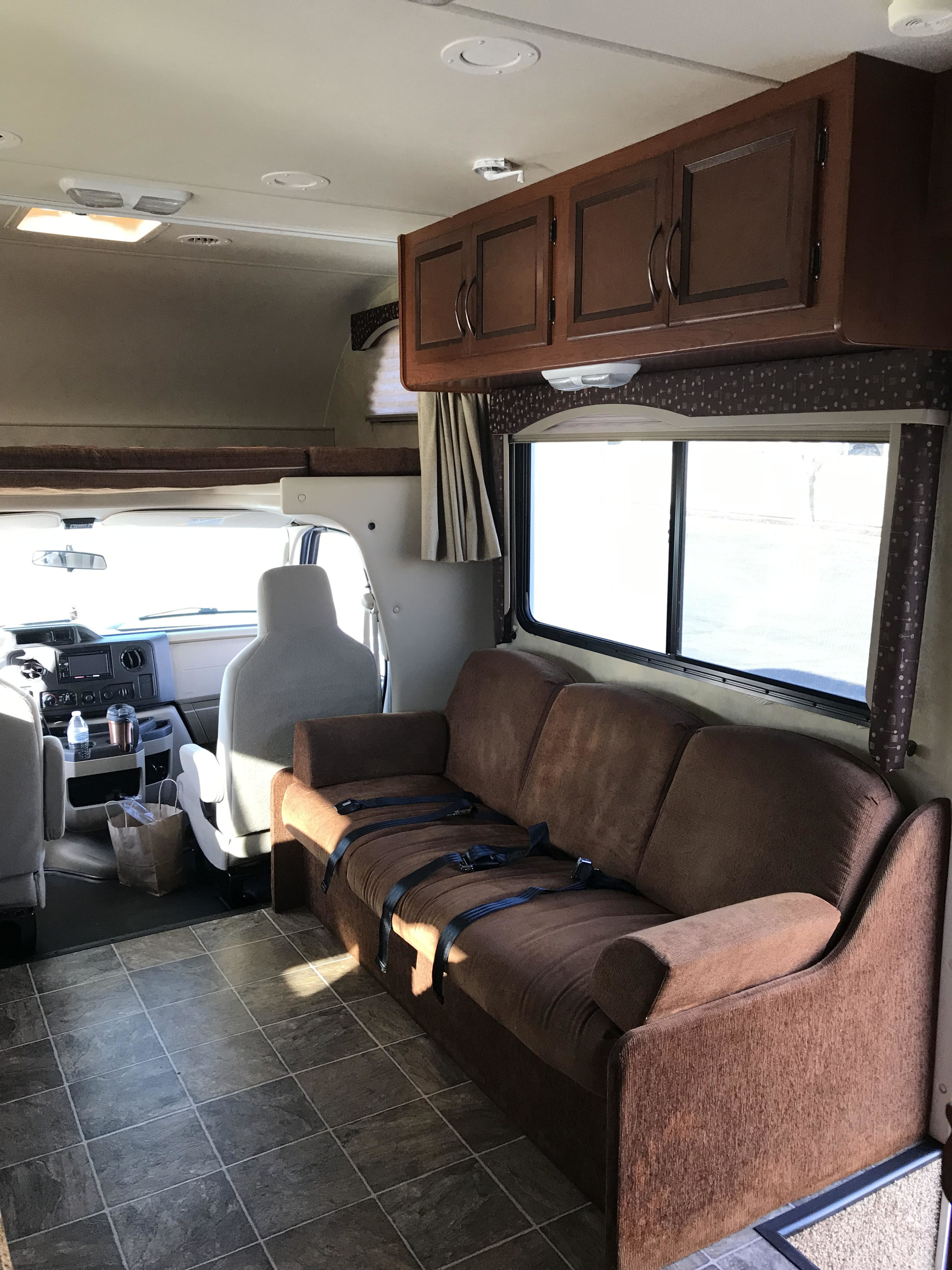 Inside a clean rv rental: a brown sofa with seatbelts, front cab, tiled floor, and overhead storage.. Thor Freedom Elite 2013