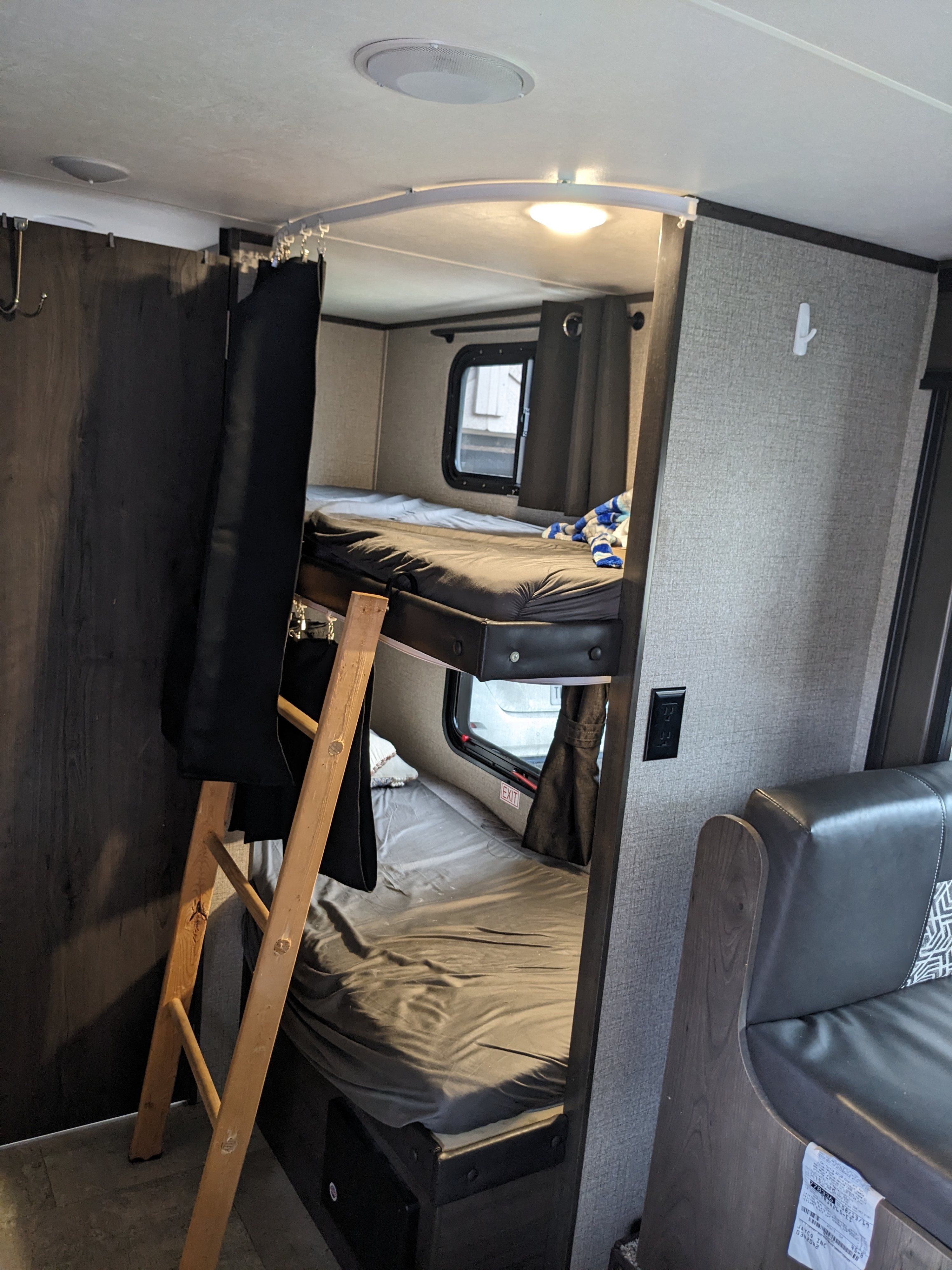 RV rental bunk beds: a cozy interior with black privacy curtains, a ladder, and a window.. Jayco Jay Flight SLX 2020