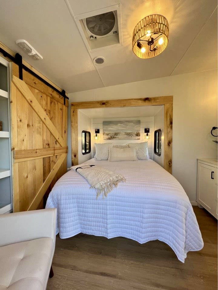 Cozy RV rental bedroom featuring a white quilted bed, rustic wooden barn door, and ambient ceiling lighting.. Fleetwood Wilderness Advantage 2004