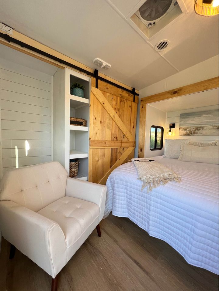 This inviting RV rental bedroom boasts a rustic barn door, built-in shelves, plush armchair, and bright white bedding.. Fleetwood Wilderness Advantage 2004