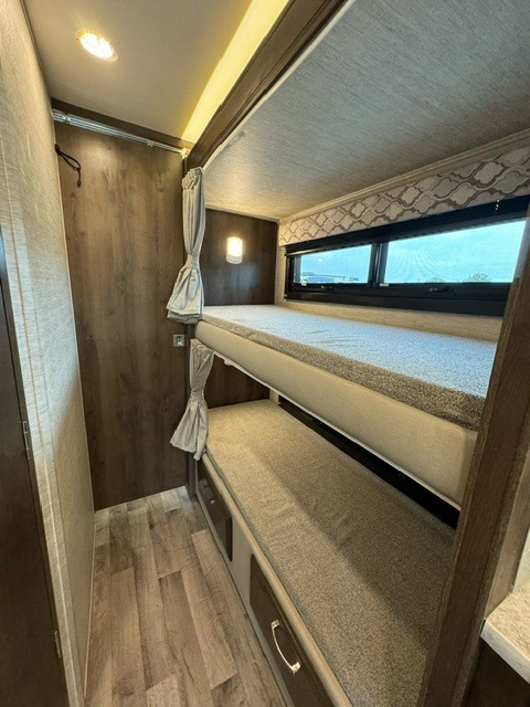 This RV rental bunk bed area features cozy sleeping spaces with a window, drawers, and warm lighting, ideal for family travel.. Jayco Redhawk 2022