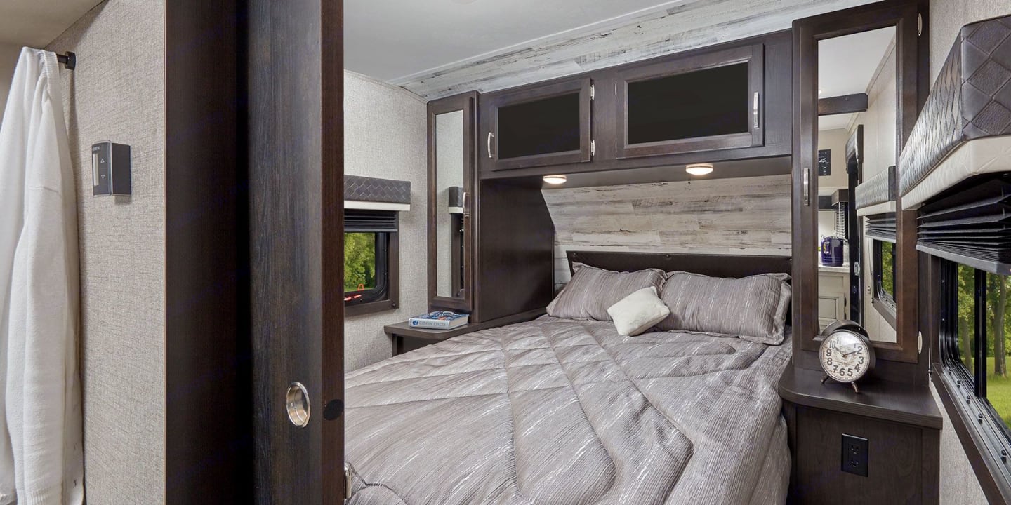 Comfortable RV rental bedroom featuring a queen bed, overhead storage, scenic window views, and an upper bunk.. Jayco Jay Feather 2021