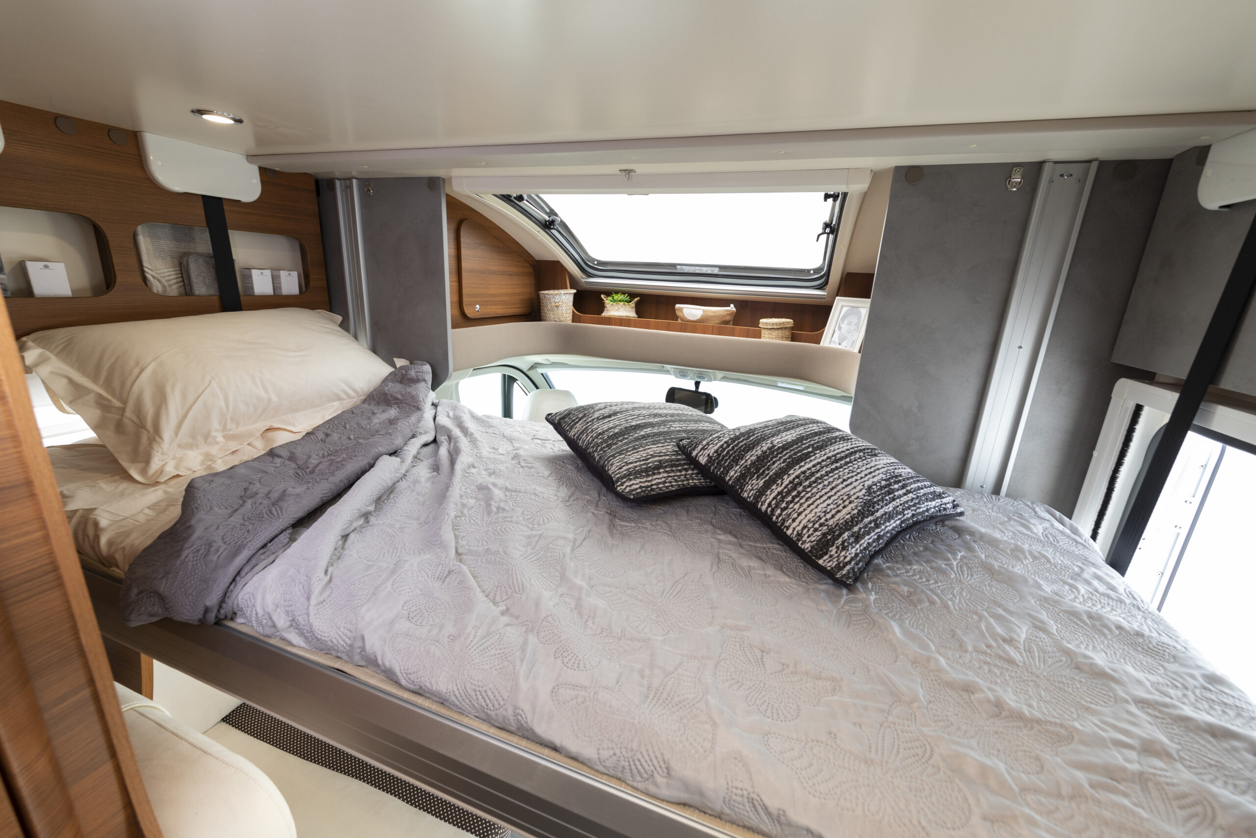 Cozy RV rental bedroom featuring a comfy bed with decorative pillows, overhead storage, and a large window above the dashboard.. Elnagh BARON 531 2023