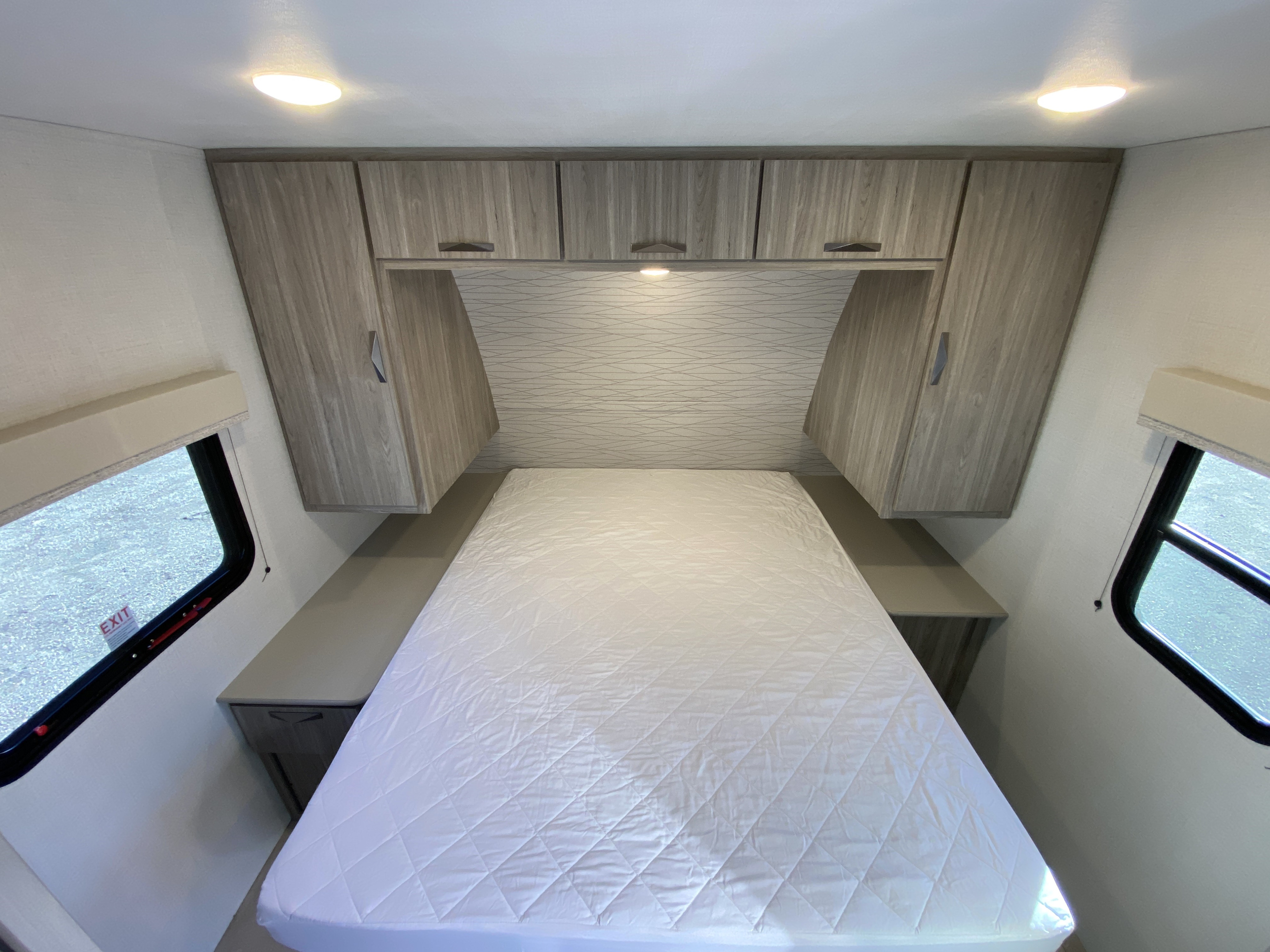 Cozy RV rental bedroom featuring a bed, overhead cabinets, and side windows with natural light.. Keystone RV Passport 2024