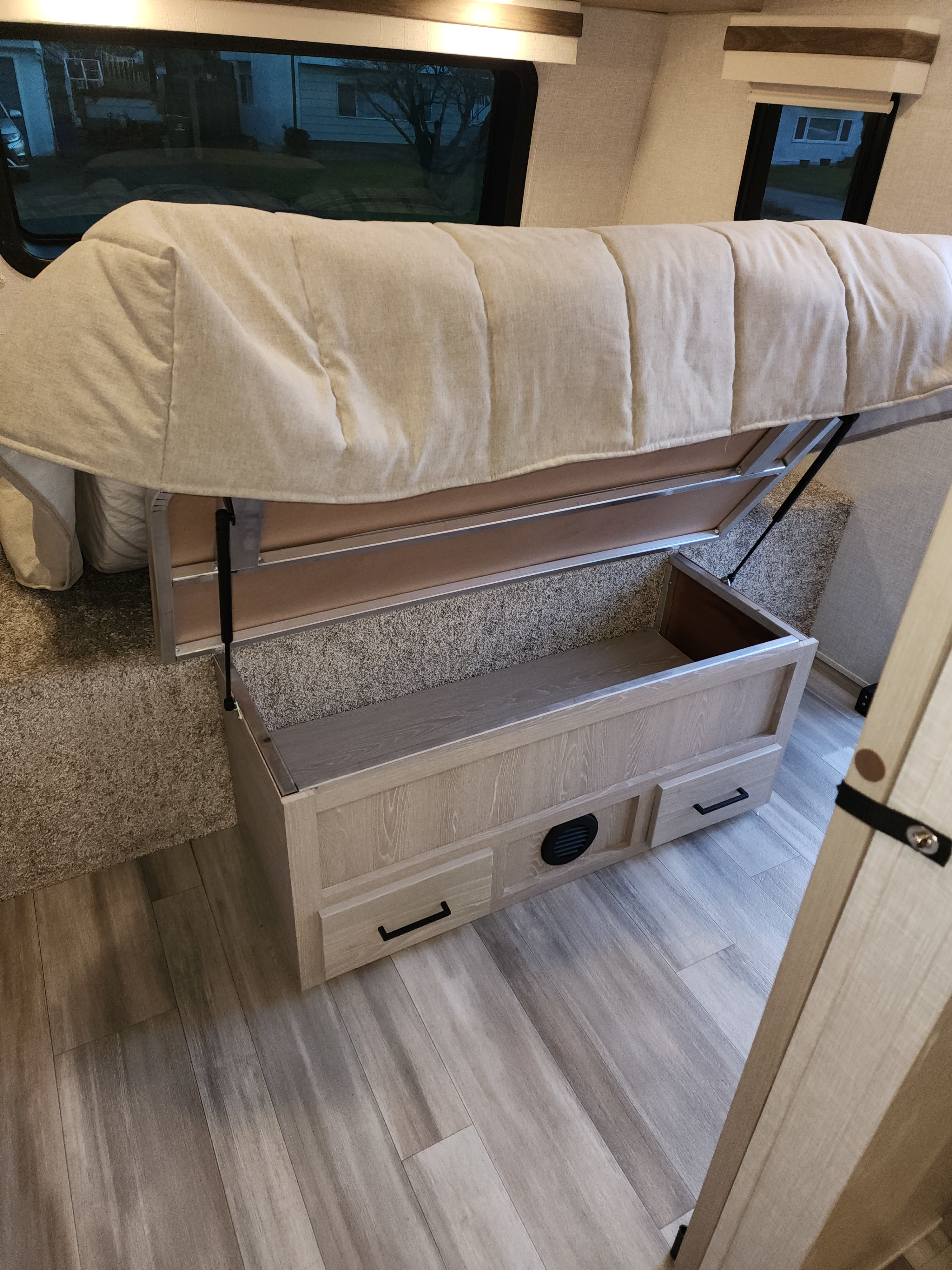 This RV rental interior features a lifted bed with gas struts for under-bed storage, a wood-toned storage bench with drawers, and a light wood-look floor.. Forest River Rockwood Ultra Lite 2022