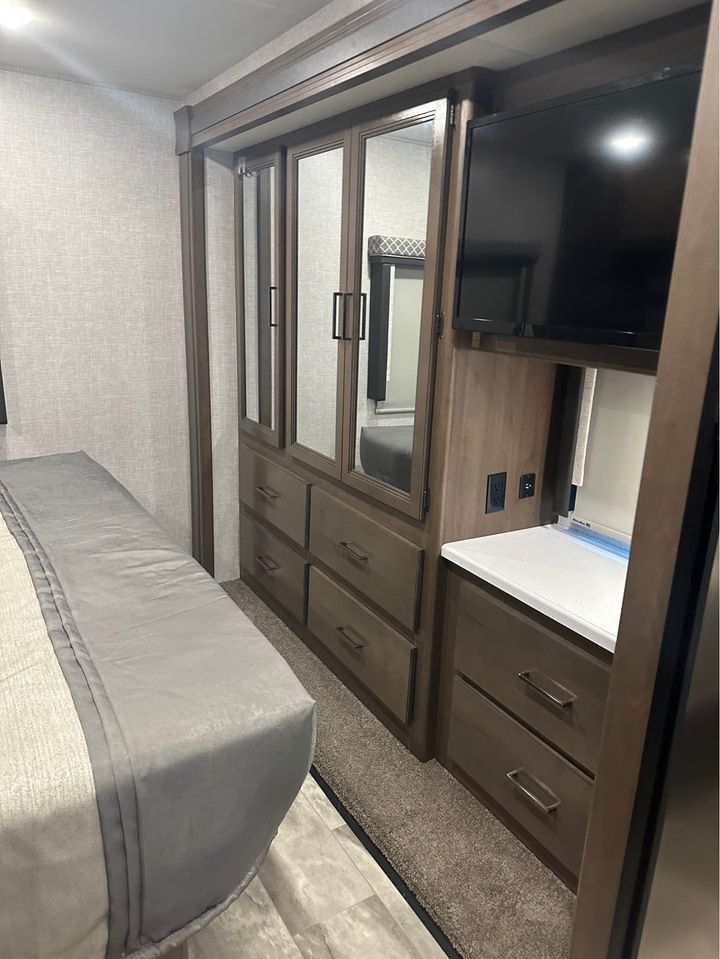 Experience a well-appointed RV rental bedroom with a comfy bed, mirrored storage, TV, and convenient built-in drawers.. Thor Windsport 2023