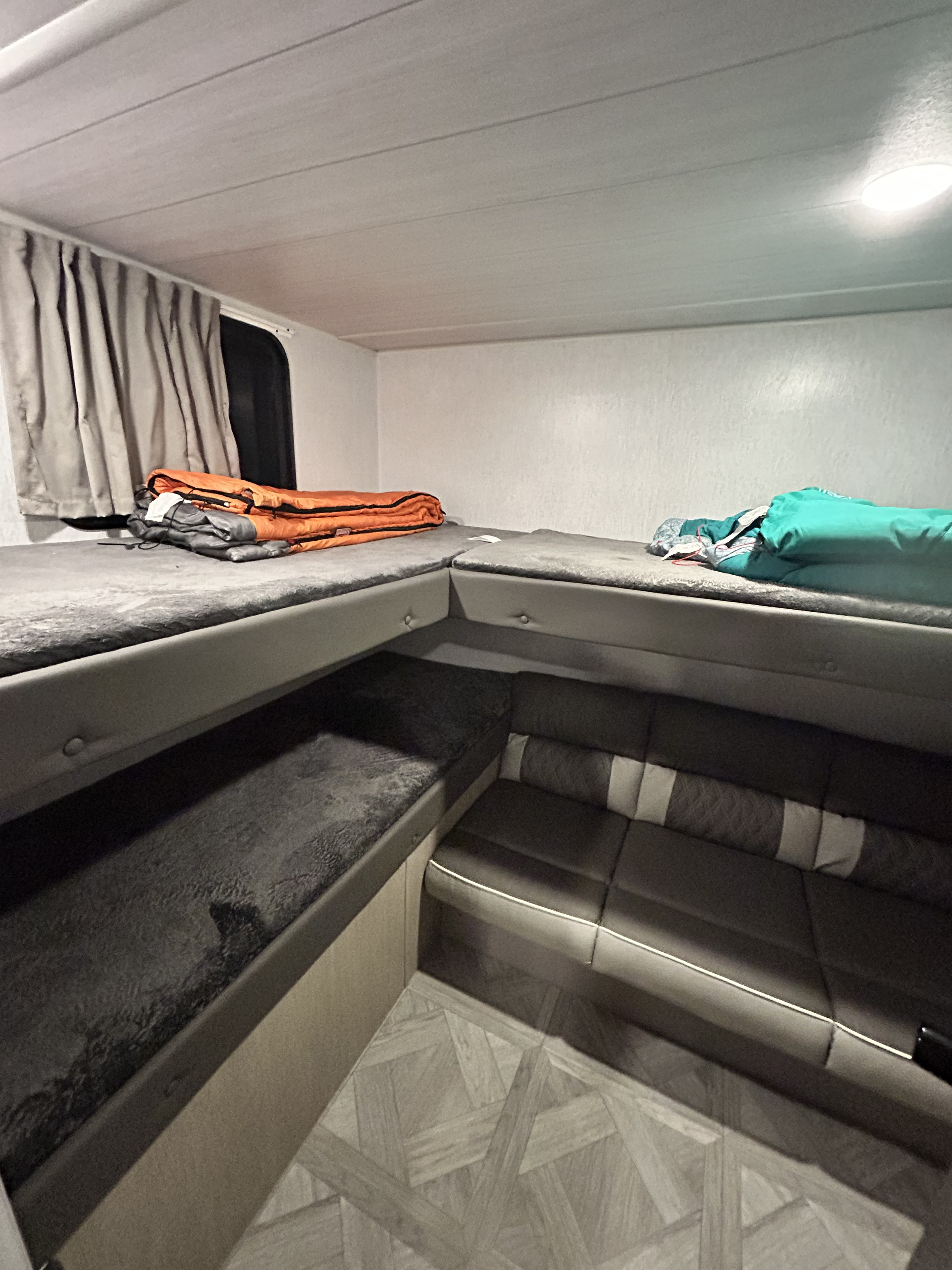 RV rental with stacked bunk beds & L-shaped seating. Features dark cushions and light walls, providing a compact sleeping & lounge area.. Forest River Wildwood X-Lite Platinum 2023