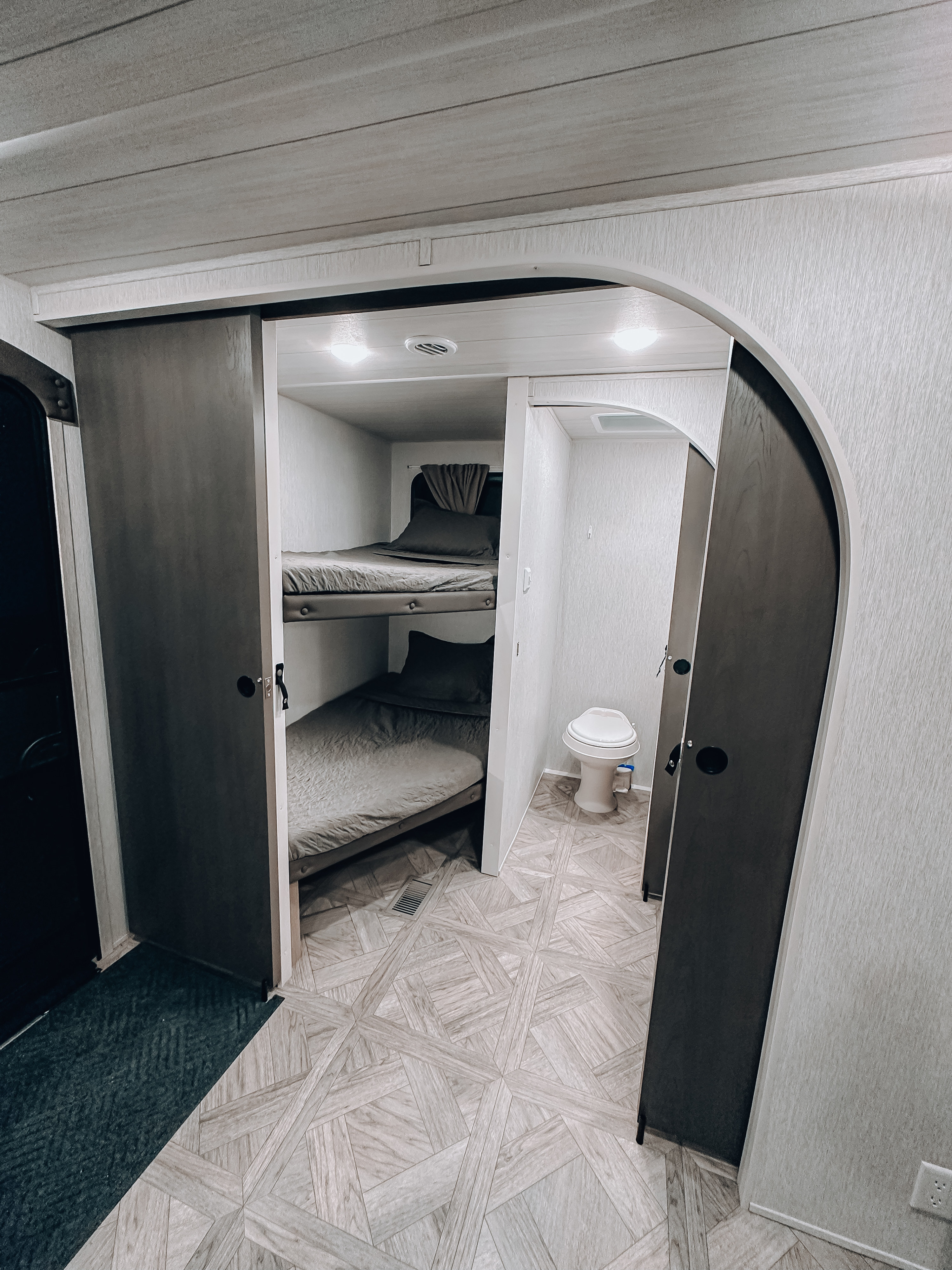 RV rental interior: cozy bunk beds next to a compact toilet area, featuring light patterned flooring.. Forest River Wildwood Platinum 2024