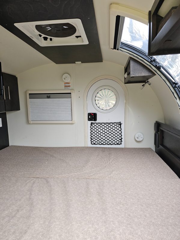 Cozy RV rental interior: large bed, round door, window with blinds, overhead vent. Perfect for adventure.. nuCamp T@G 2021