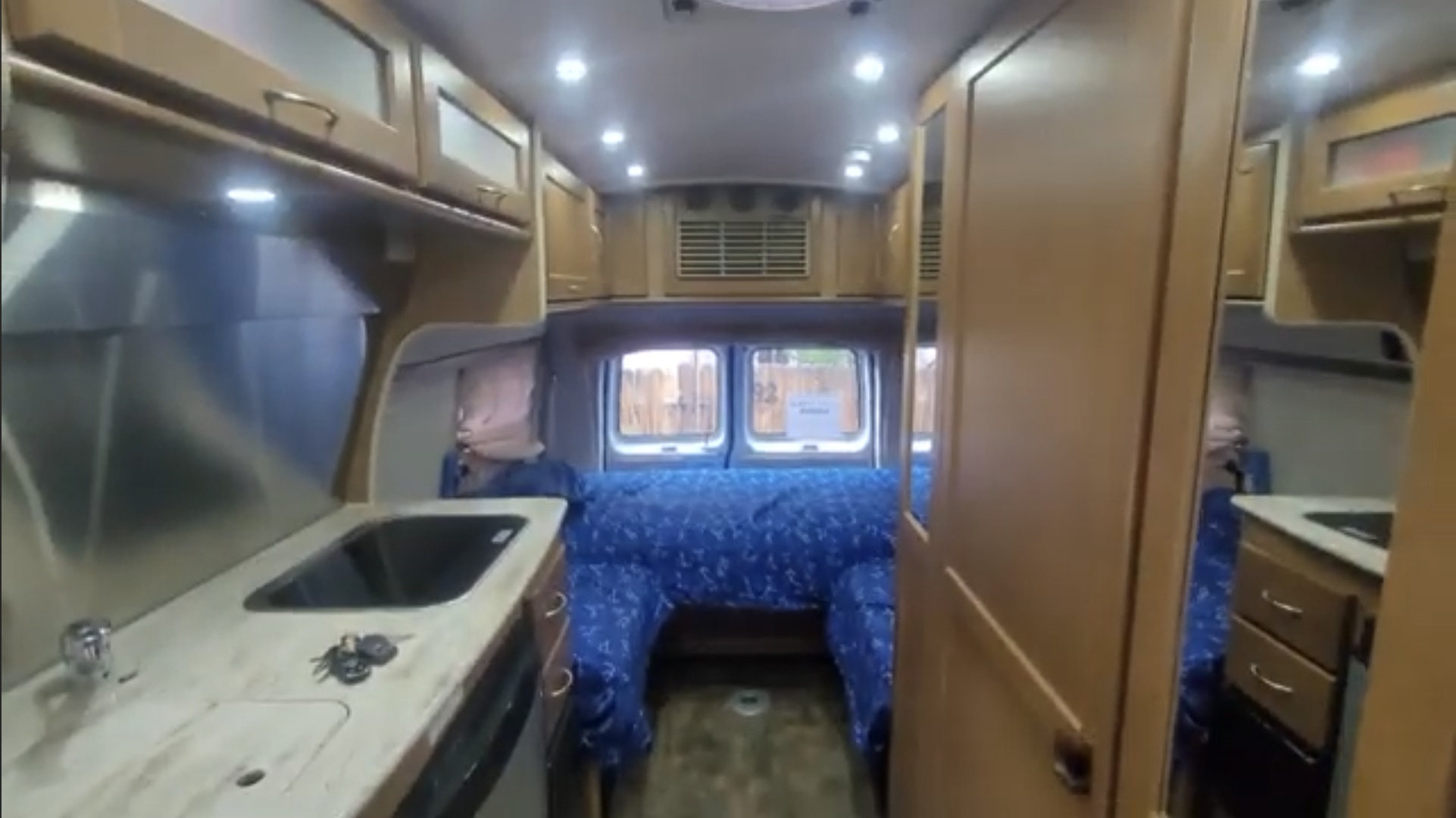 RV rental: Brightly lit camper van interior. Features a compact kitchen with sink on the left & a blue patterned bed at the rear.. Pleasure-Way Excel TS 2012