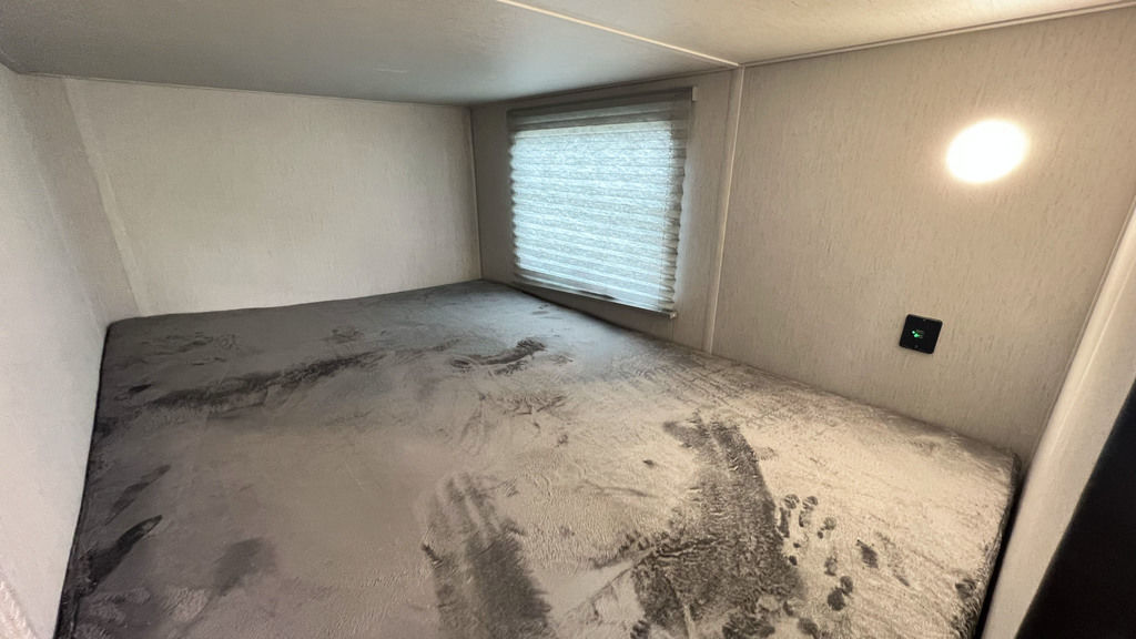 Cozy RV rental sleeping nook with gray bedding, window, and wall-mounted light and charging port.. Forest River Cherokee Grey Wolf Black Label 2023