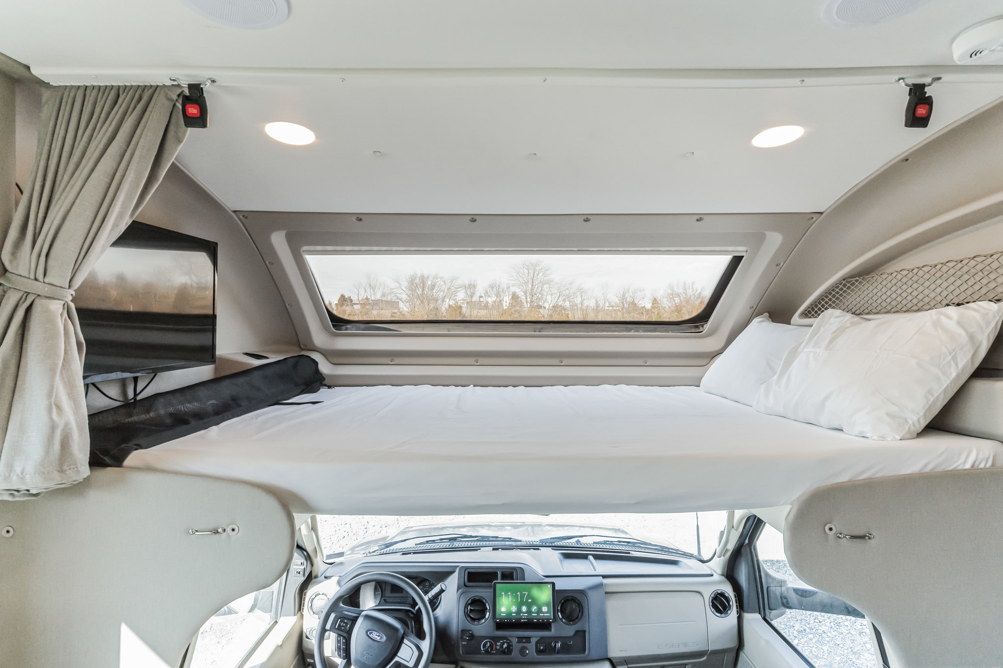 Explore this RV rental's cozy cab-over bunk with bedding, TV, and panoramic window above the modern cockpit.. Entegra Coach Esteem 2023