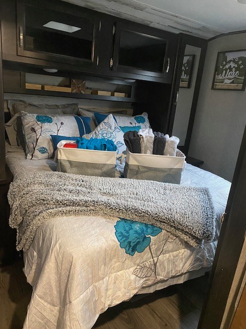 This RV rental bedroom features a cozy bed with floral bedding, gray blanket, and overhead cabinets. Organized storage.. Jayco Jay Feather 2021