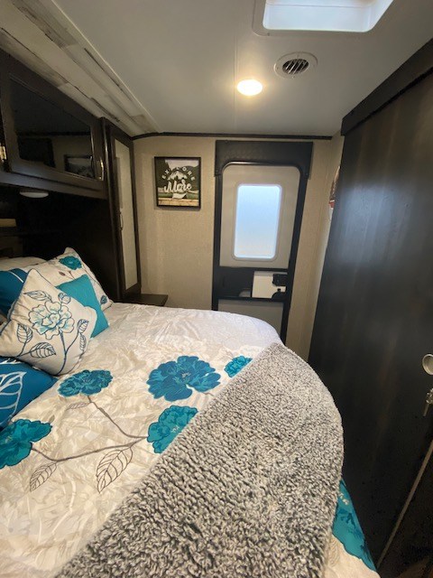 Cozy RV rental bedroom interior featuring floral bedding, a grey blanket, and "Explore More" wall art. Ideal for travel.. Jayco Jay Feather 2021