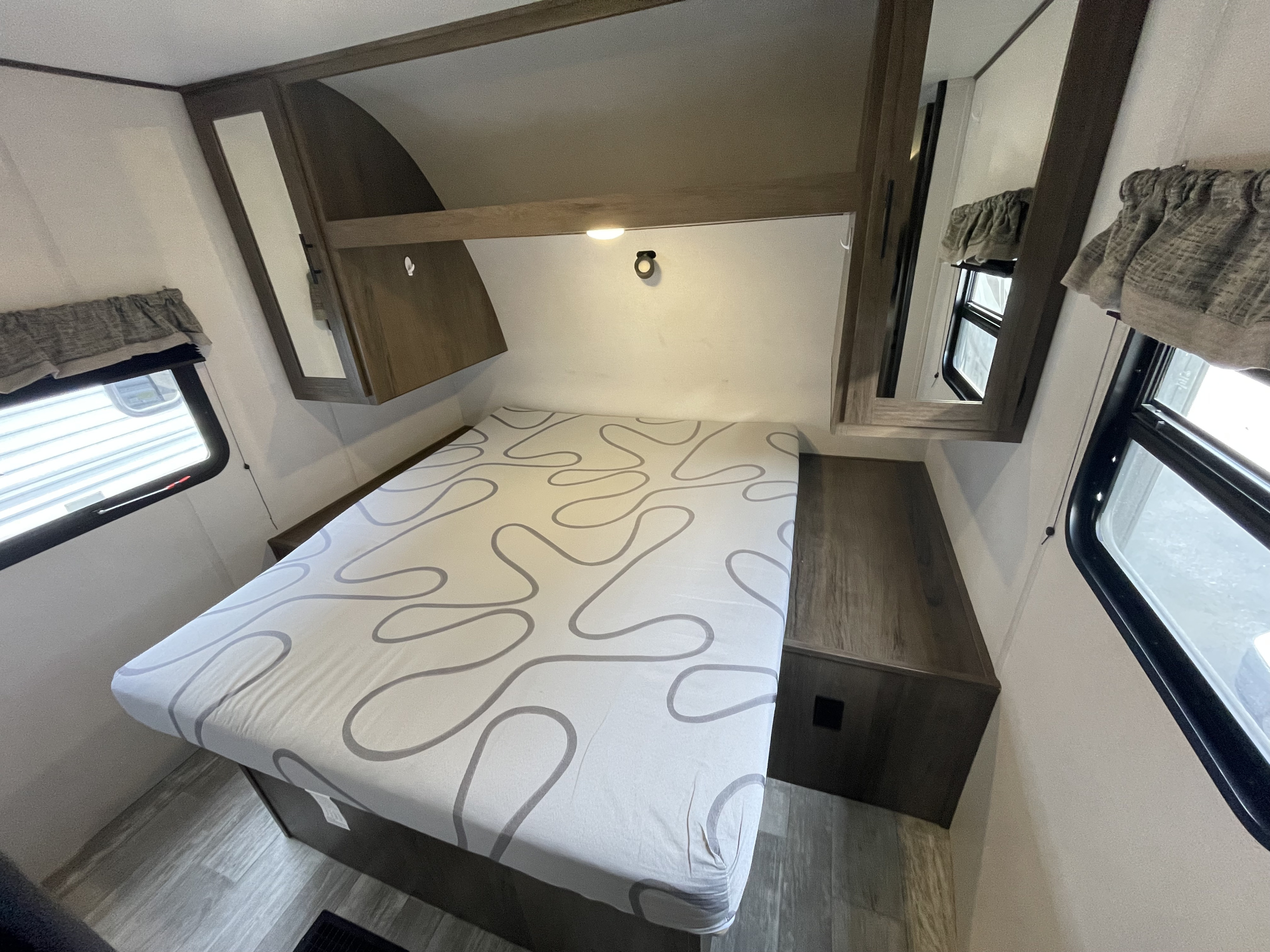 RV rental bedroom featuring a patterned bed, built-in wooden storage, and side mirrors, ready for a comfortable journey.. Forest River Avenger 26DBSLE 2021