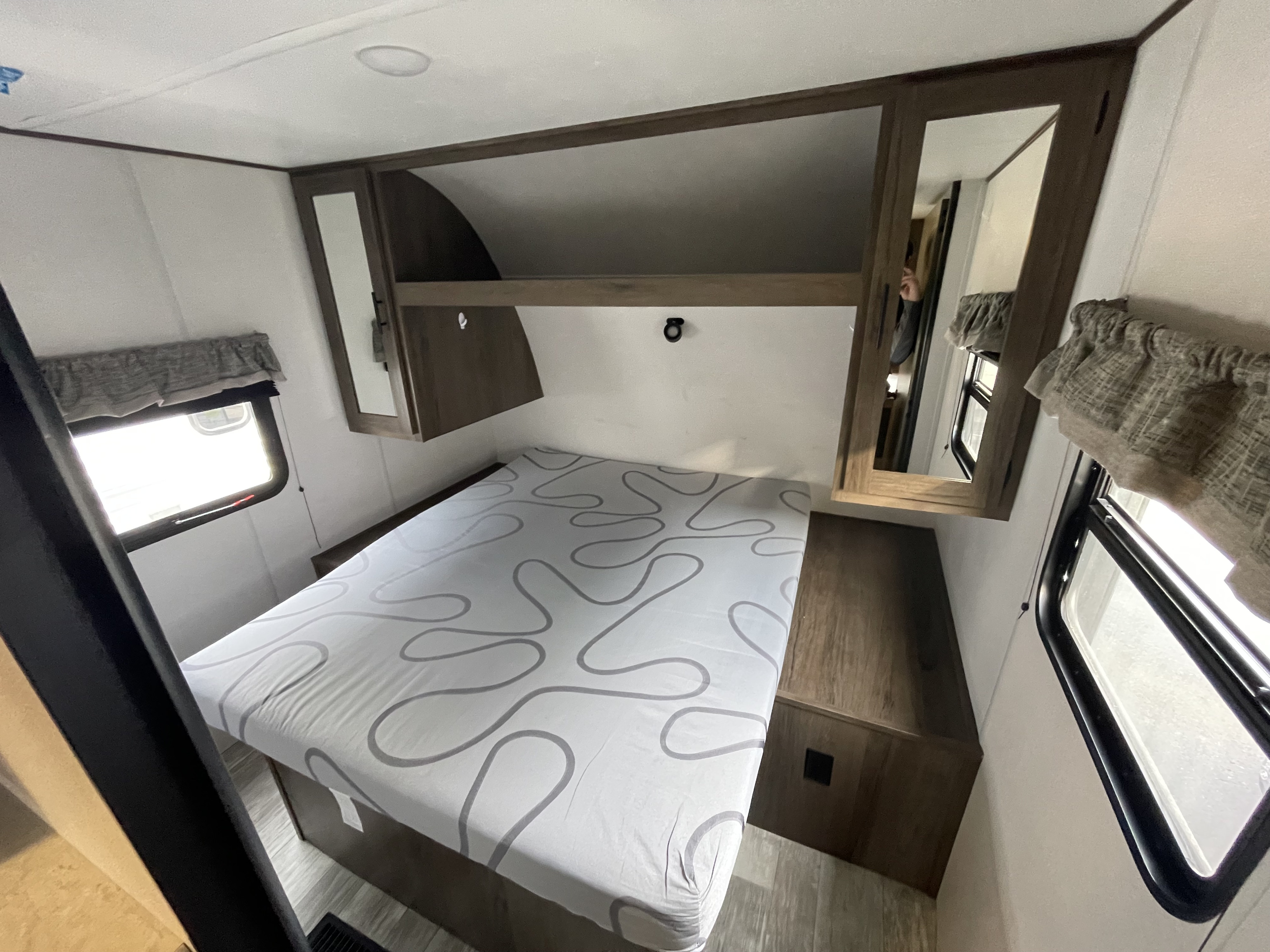 RV rental bedroom with patterned bed, mirrored cabinets, and windows, offering comfortable travel accommodation.. Forest River Avenger 26DBSLE 2021