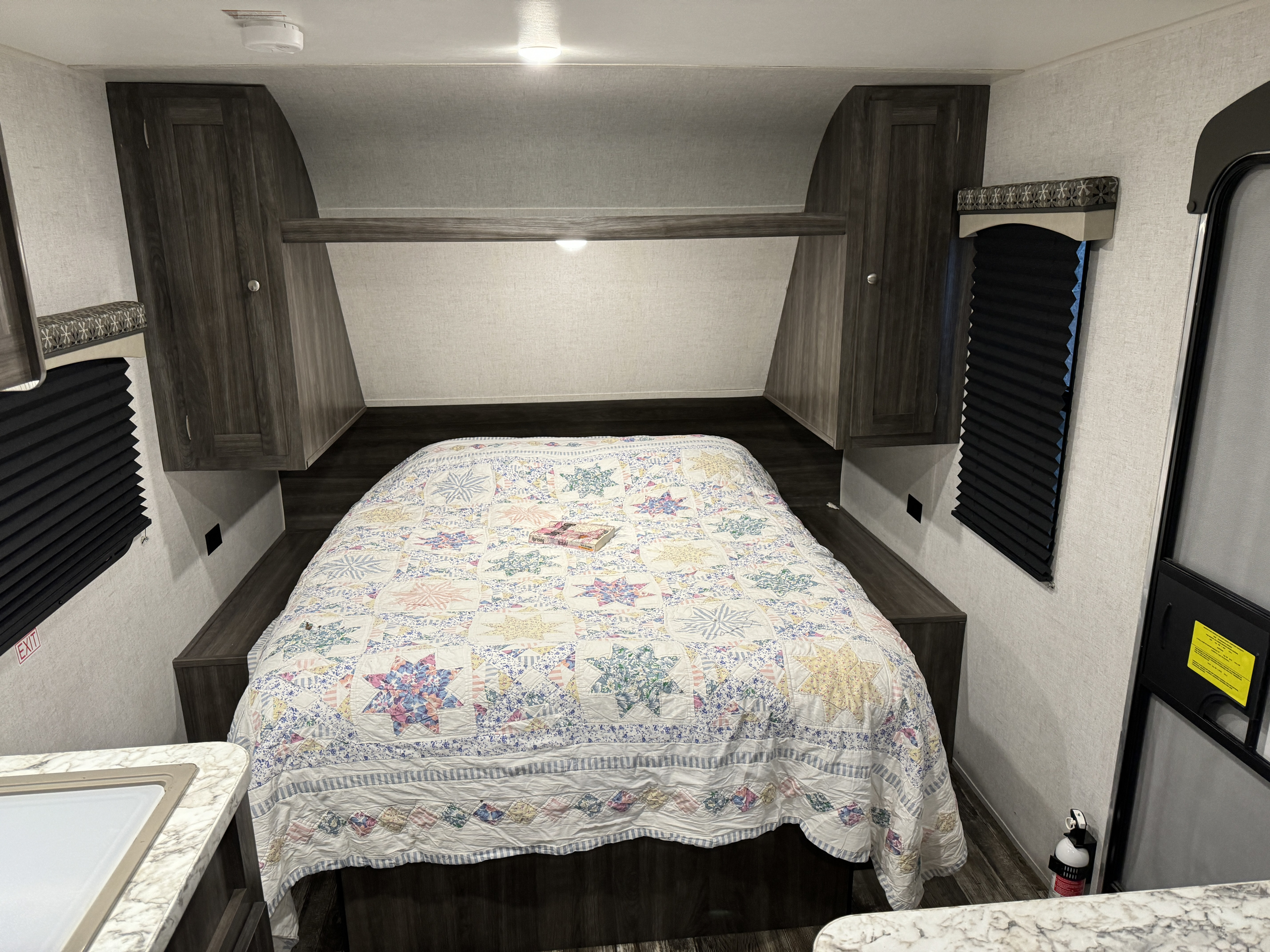 RV rental interior: A bright bedroom with a colorful quilt, storage cabinets, and natural light from windows.. Starcraft Autumn Ridge Outfitter 2020
