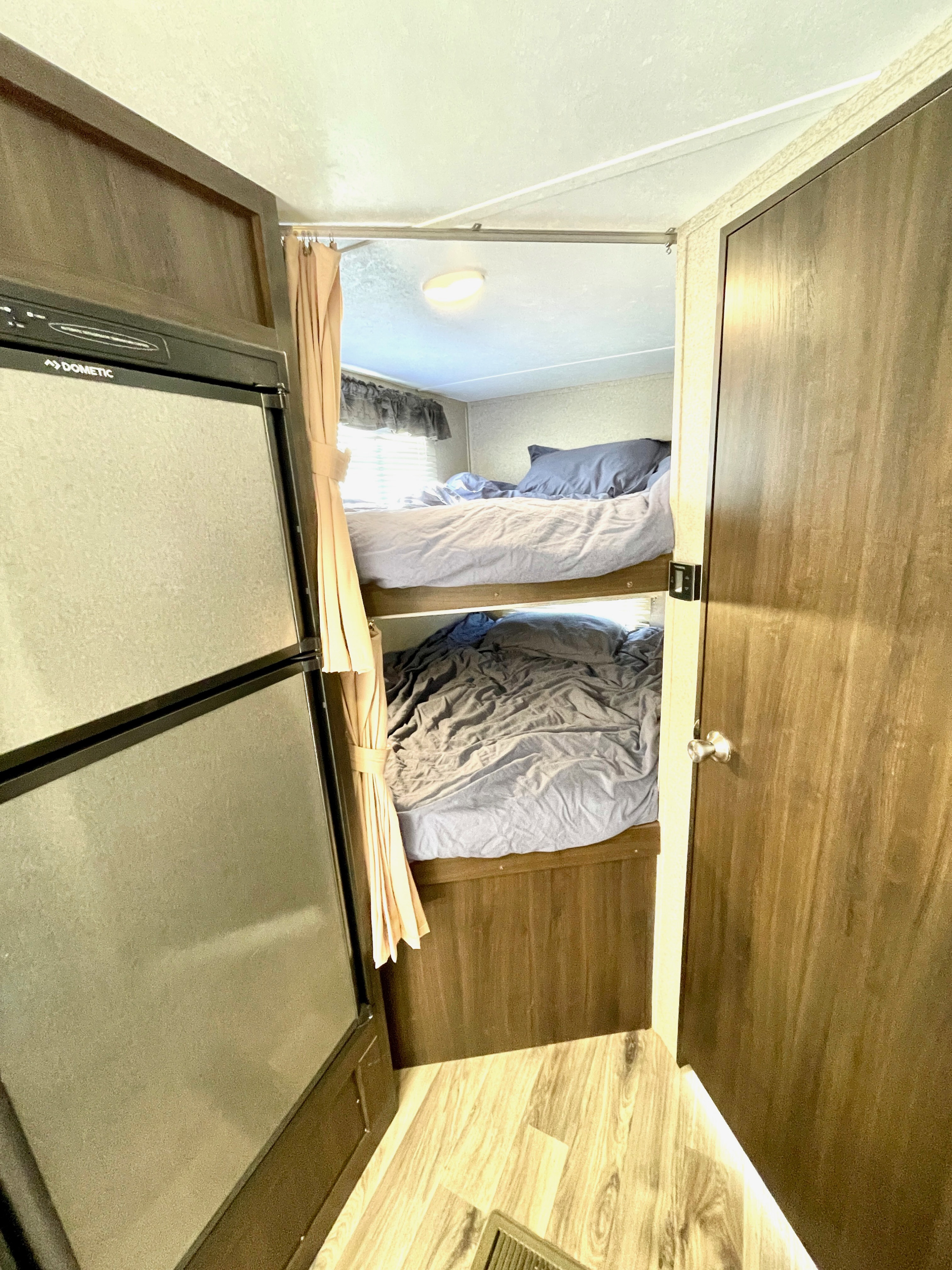 RV rental interior: bunk beds with bedding next to a Dometic fridge. A doorway is on the right, offering comfy travel stays.. Keystone RV Springdale Eco-Lite 2018
