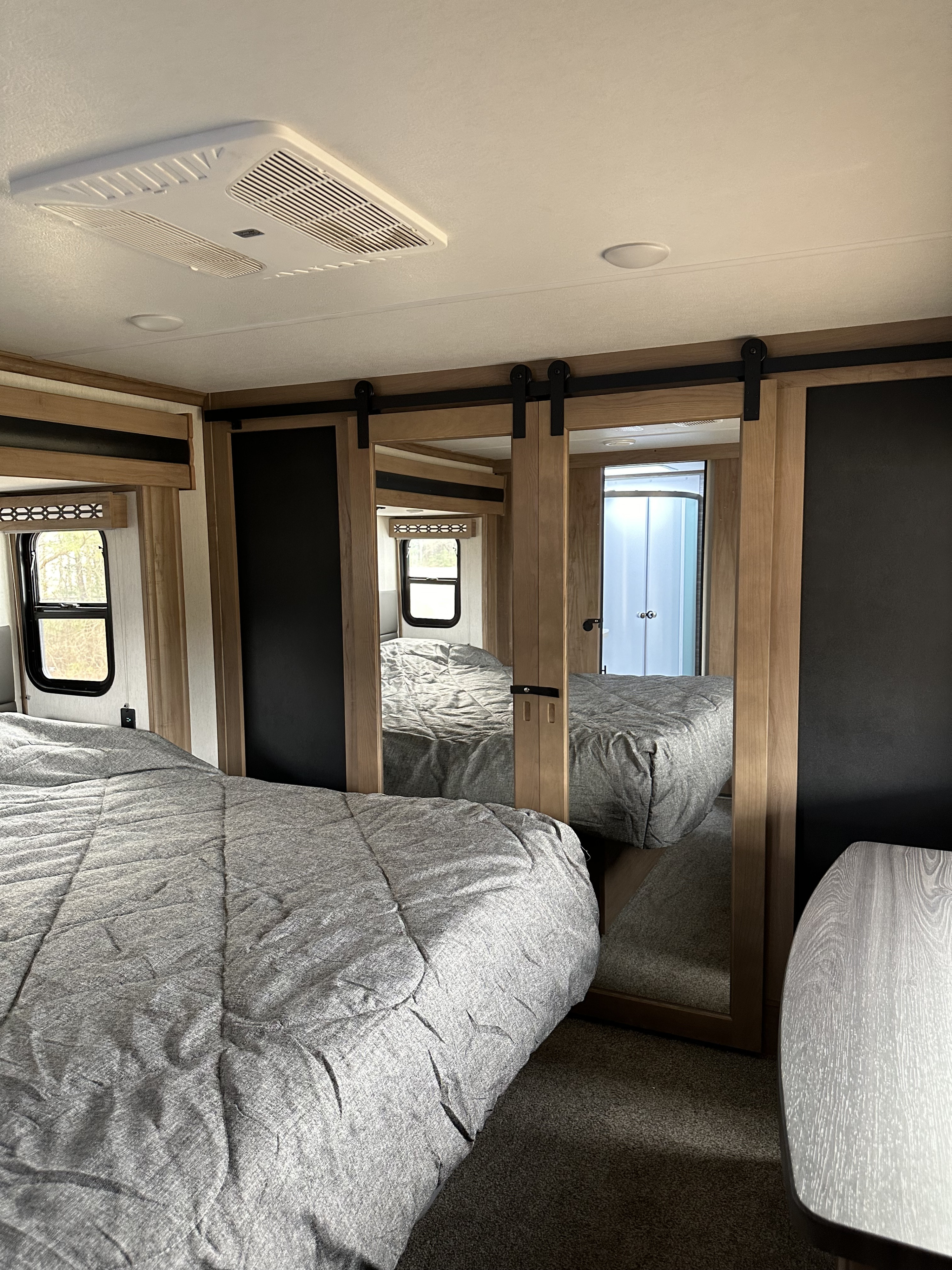 Cozy RV rental bedroom: grey bed, mirrored barn doors revealing a shower, and ceiling AC. A comfortable travel space.. Forest River Vengeance Rogue Amored Toy Hauler 2023