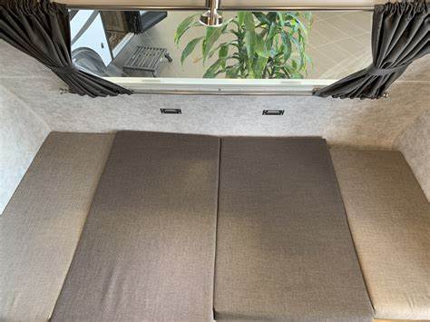 Cozy RV rental interior shows a multi-section bed and window with tied-back curtains, offering a nature view.. Prolite E-Volt 2021