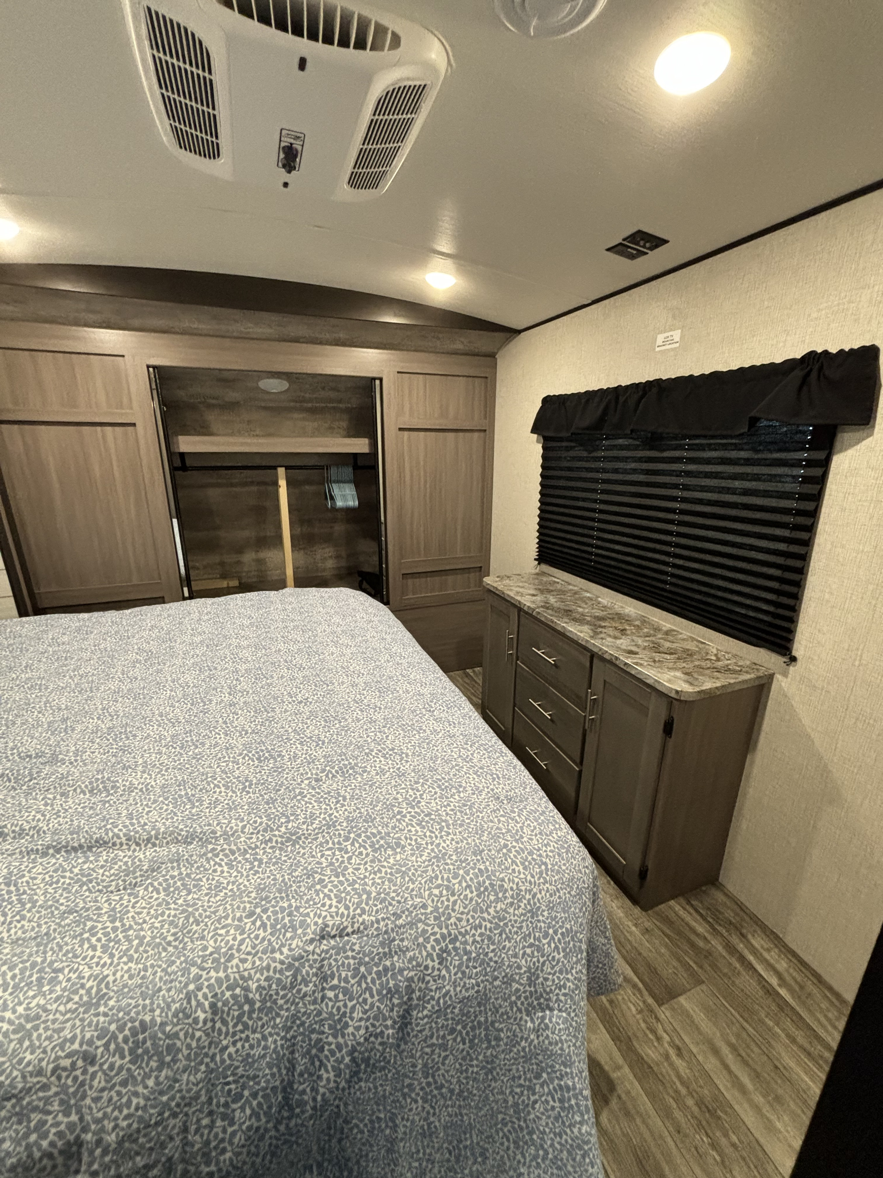 Comfortable RV rental bedroom with patterned bed, open closet, dresser, window, and ceiling AC.. Crossroads RV Sunset Trail Super Lite 2023