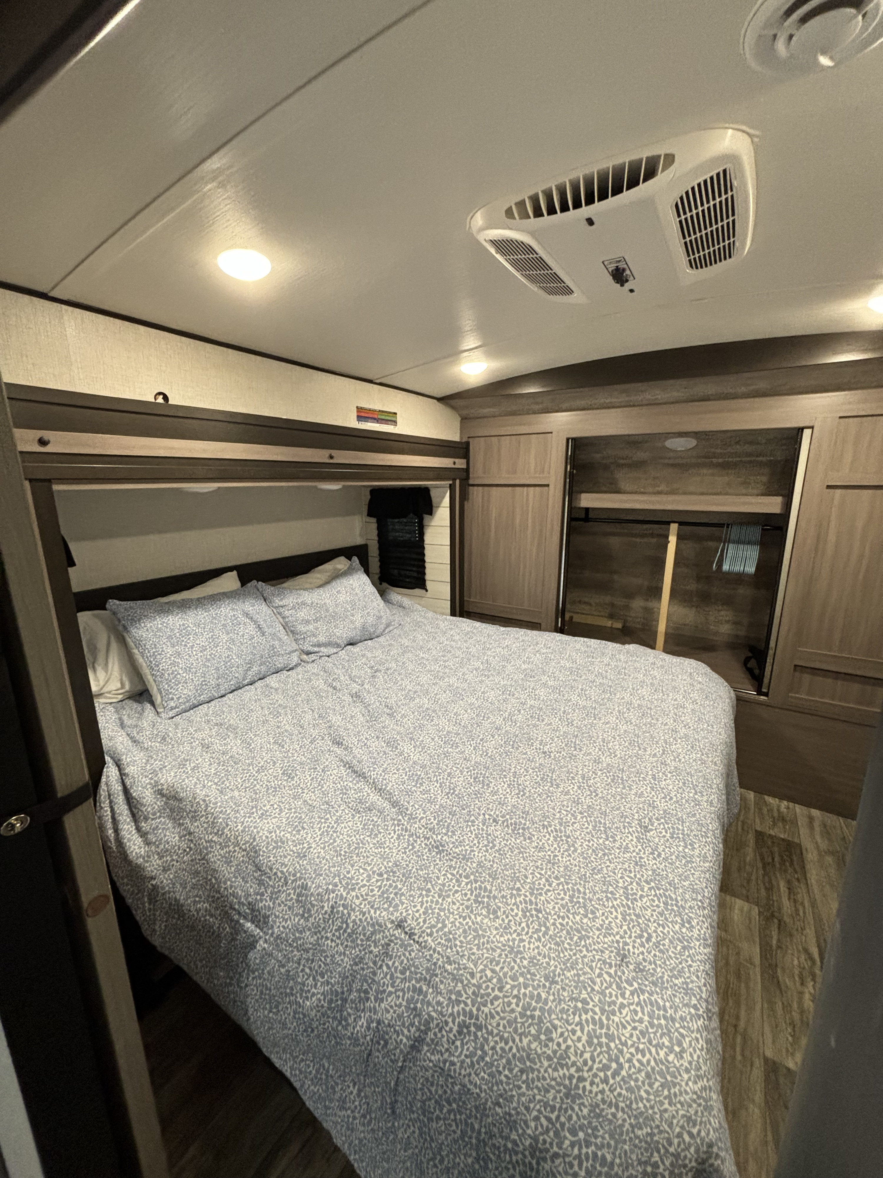 This RV rental bedroom features a comfortable bed with patterned bedding, built-in storage, and an AC unit for a cozy stay.. Crossroads RV Sunset Trail Super Lite 2023