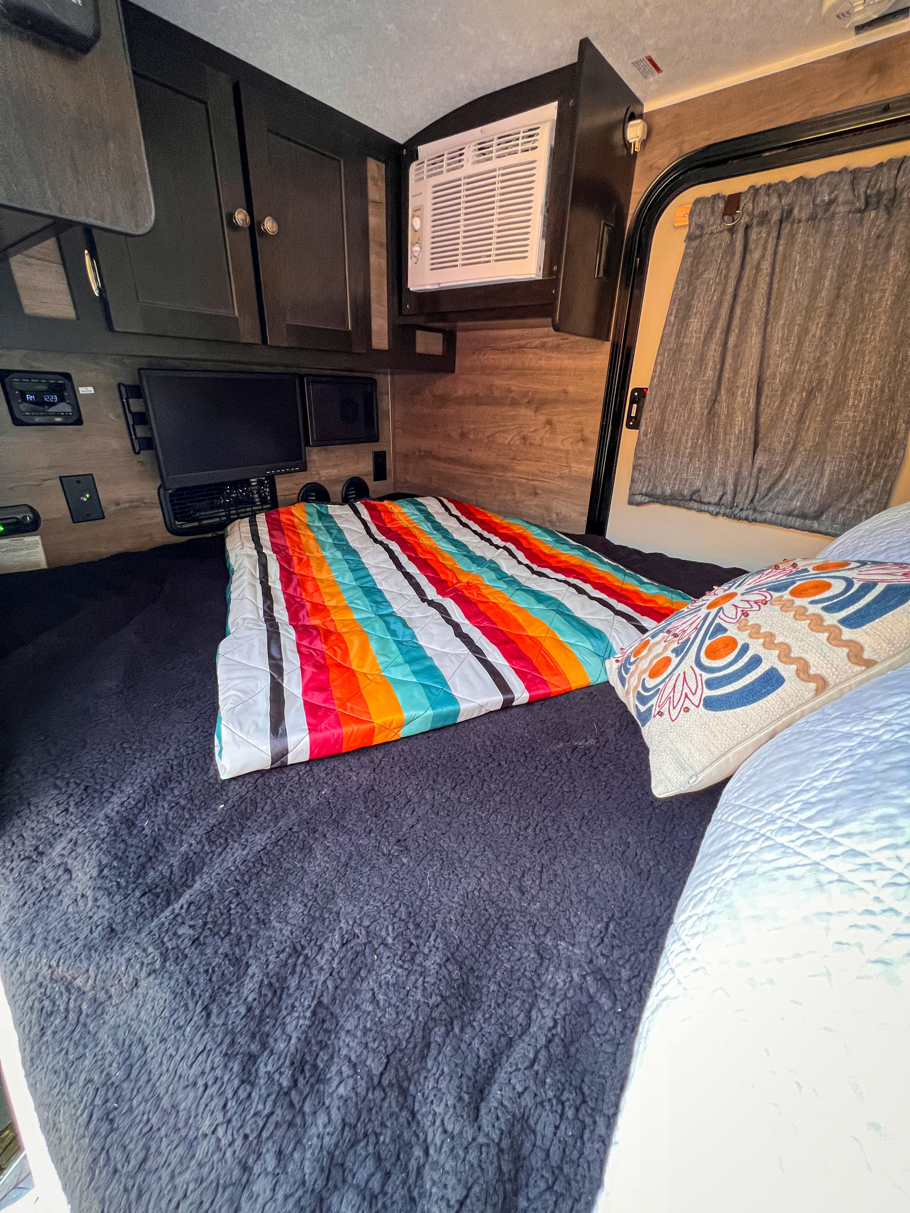 Cozy RV rental interior featuring a bed with a vibrant striped blanket, wall-mounted TV, and overhead AC.. Braxton Creek Bushwhacker 2022