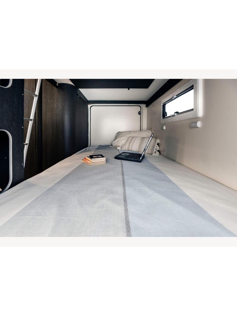 Inside an RV rental: a compact sleeping area with a long bed, striped sheets, pillows, a laptop, and books. A window is on the right.. Roller Team Zefiro 675 2023