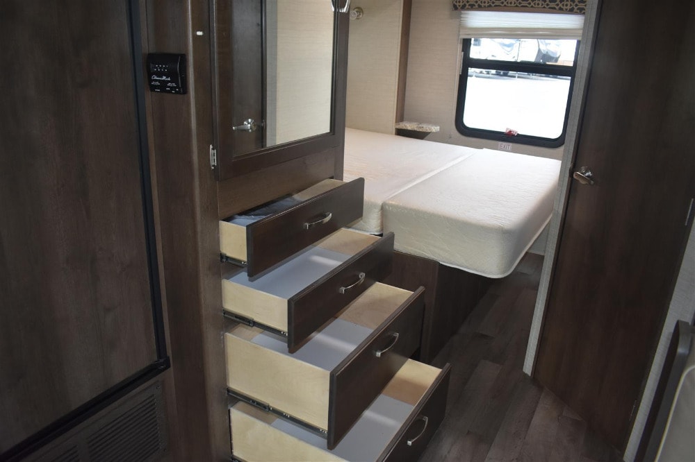 RV rental: A cozy bedroom with dark wood finishes, featuring a bed, mirrored cabinet, and efficient storage drawers.. Jayco Redhawk 2019