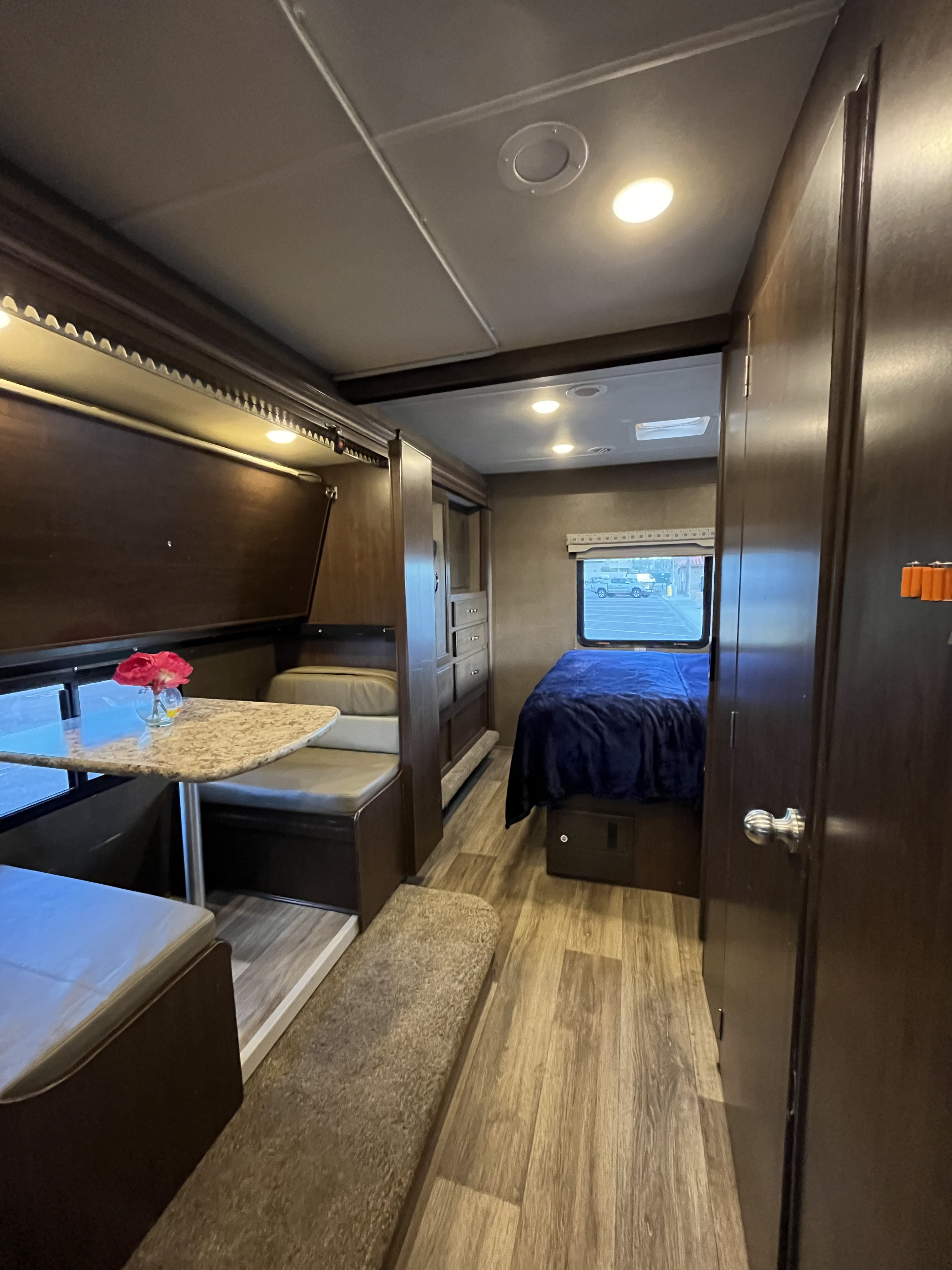 Cozy RV rental interior featuring a bright dinette with red flowers, comfortable bedroom with blue blanket, and warm wood accents.. Thor Motor Coach Freedom Elite 2018