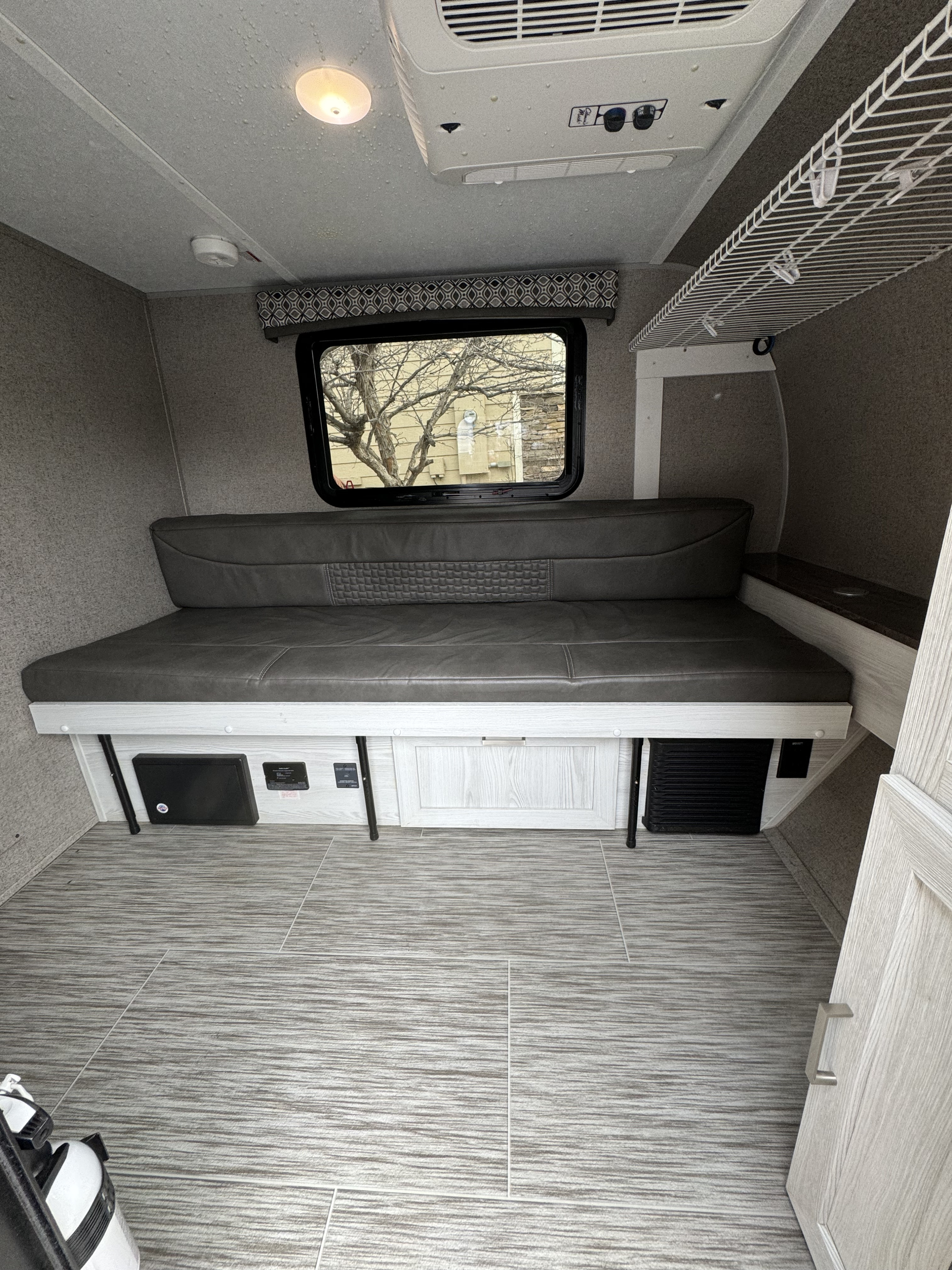 Cozy RV rental interior with a gray sofa bed, large window, ceiling AC unit, and light wood-tone flooring and cabinetry.. Forest River Rockwood Geo Pro 2019