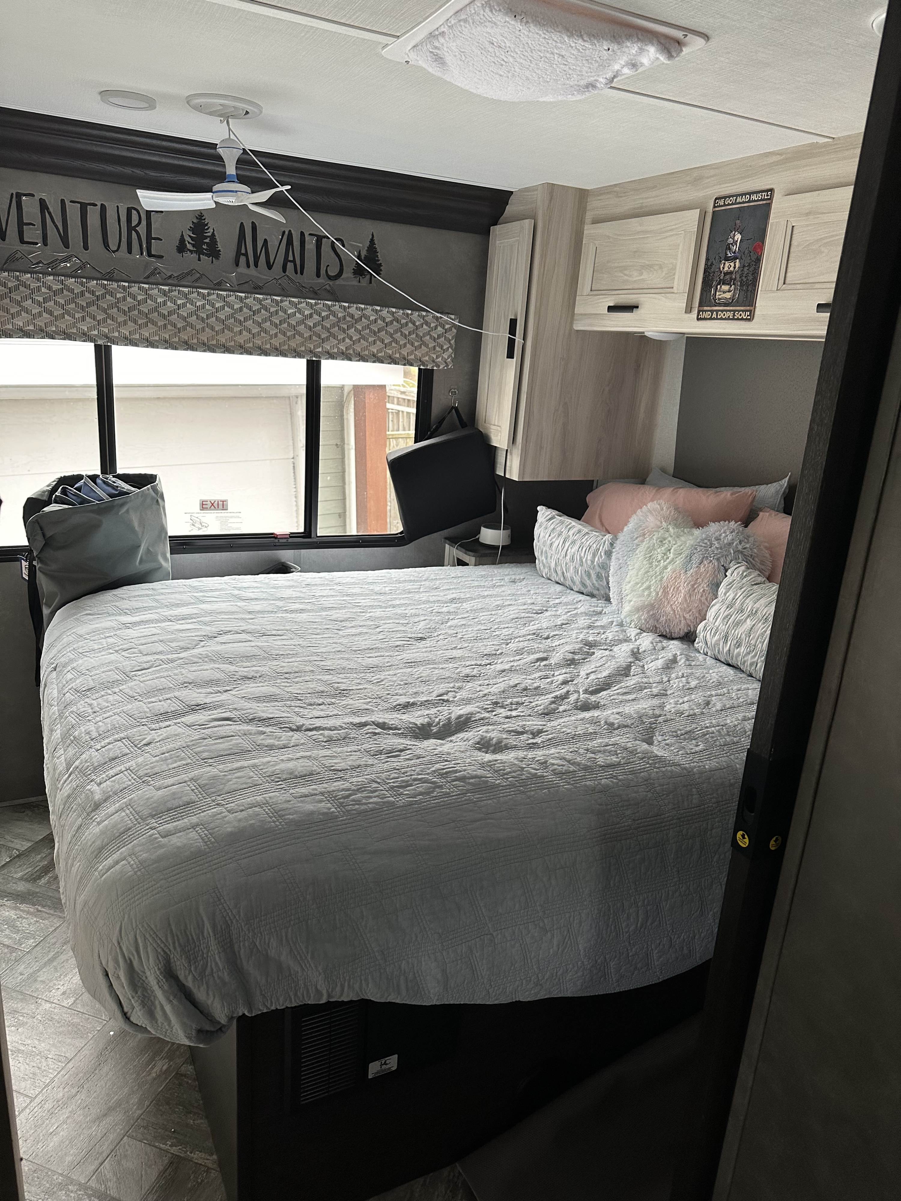 Compact RV rental bedroom featuring a bed with colorful pillows, an overhead fan, and an "Adventure Awaits" wall decal.. Forester LE 2022