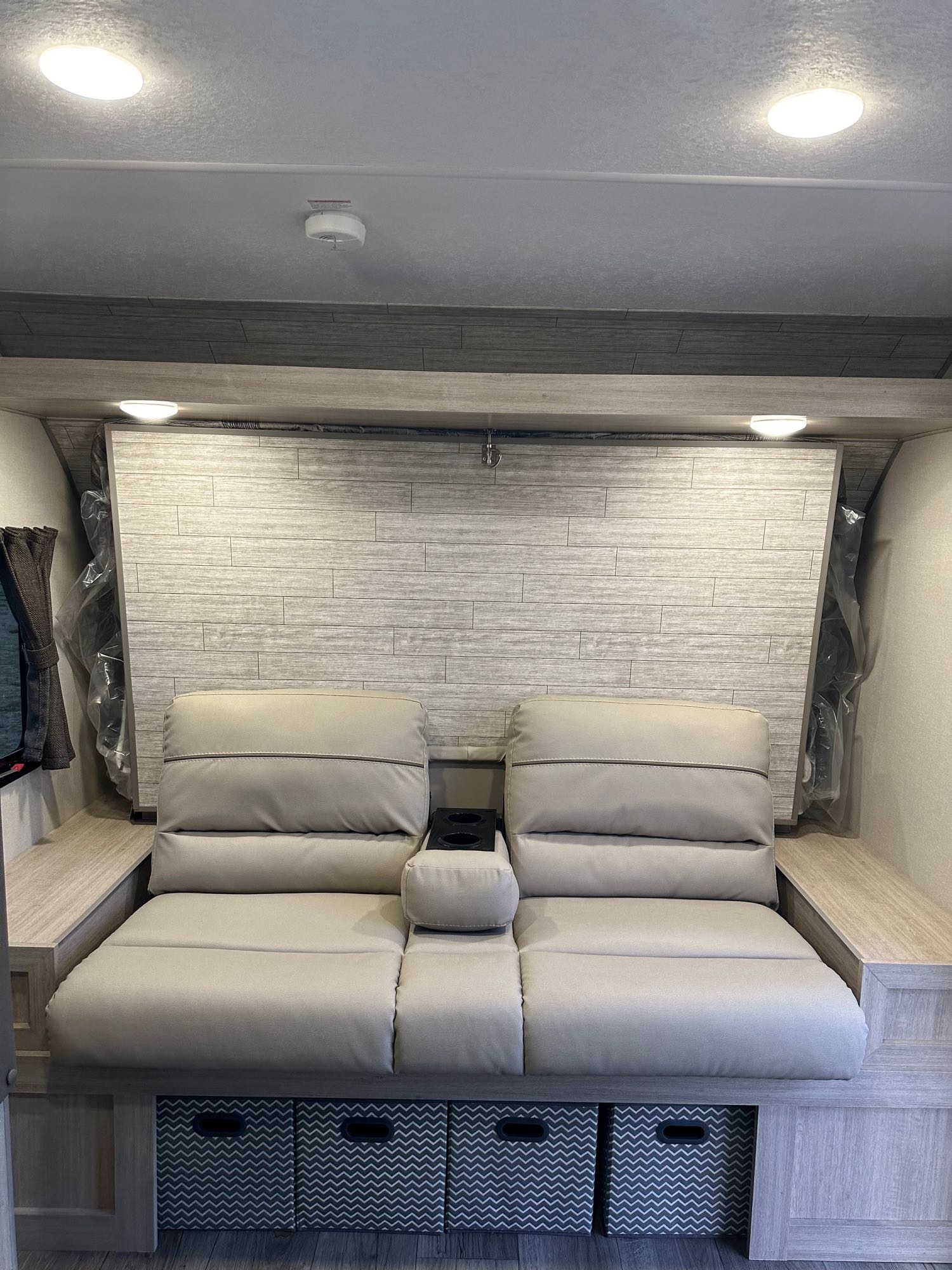 Modern RV rental interior: light sofa/bed with recliners, cup holders, and chevron storage bins. Ideal for compact living.. Coachmen RV Catalina Summit Series 7 2024