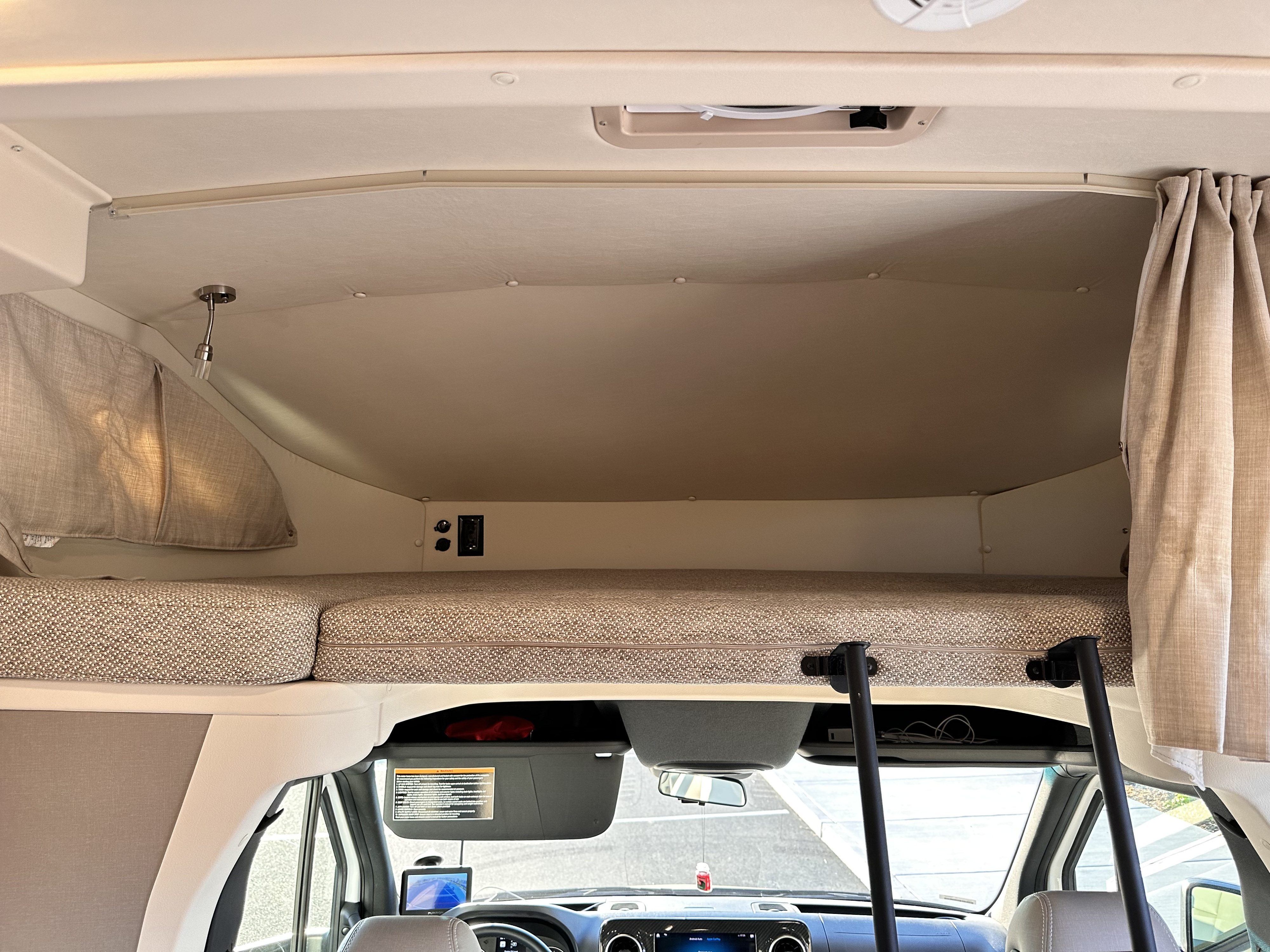 RV rental interior: A comfortable over-cab bunk bed with mattress, privacy curtains, and charging ports.. Winnebago Navion 2023