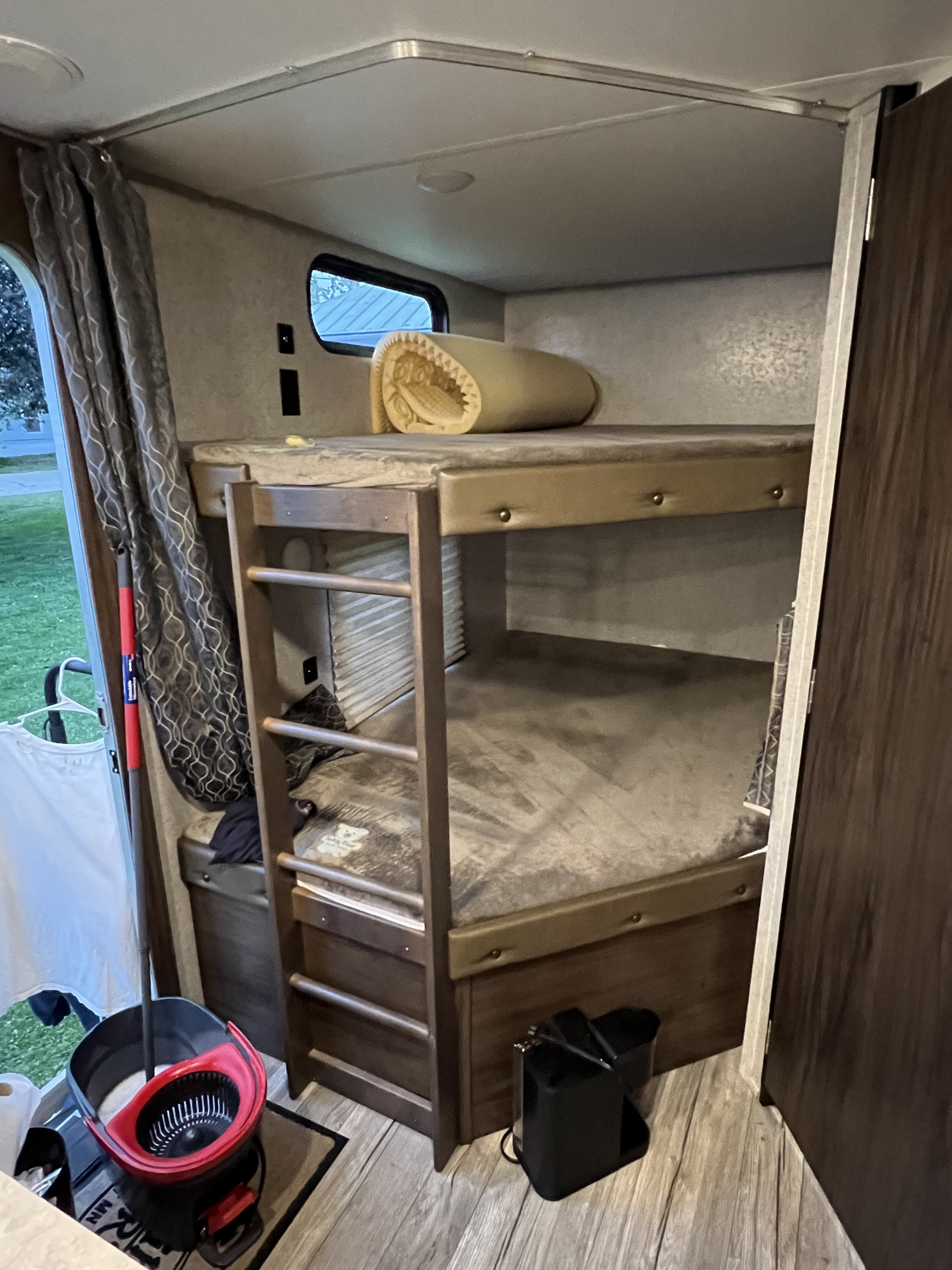 Cozy bunk beds in an RV rental, featuring a ladder, window with curtains, and a rolled mattress. Interior shows a functional space.. Forest River Cherokee 2019