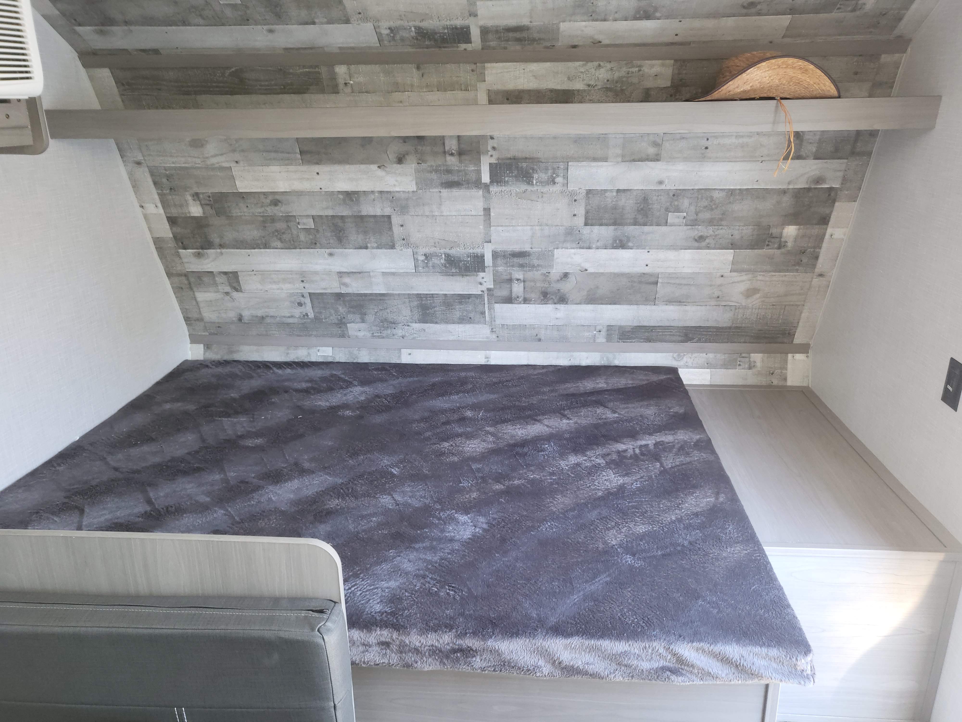 Cozy RV rental bedroom featuring a grey bed, wood-paneled wall, and a shelf with a straw hat, ideal for travel.. Dutchmen Coleman Lantern LT 2023