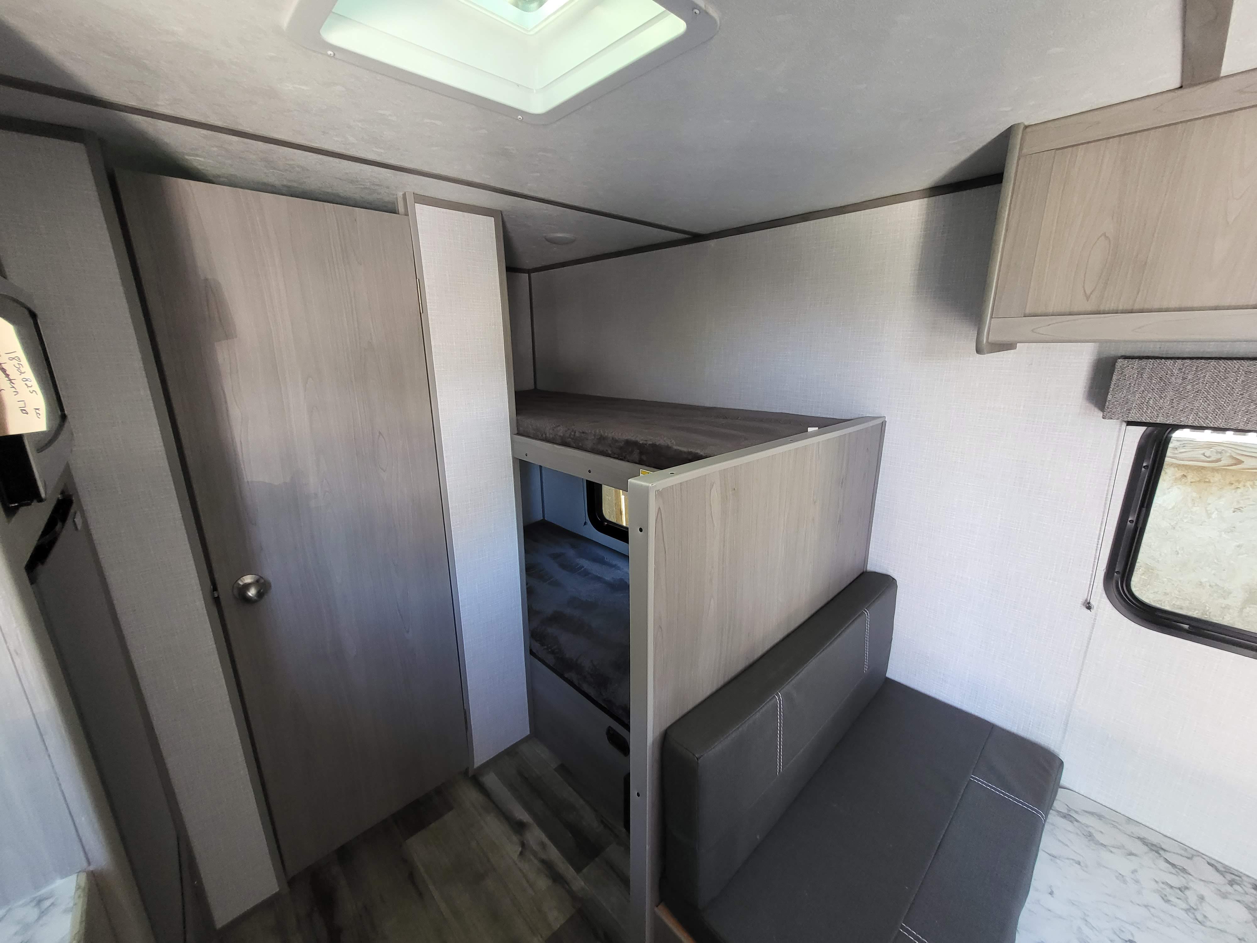 RV rental interior showing bunk beds, a storage closet, seating area, overhead cabinets, and a window view.. Dutchmen Coleman Lantern LT 2023