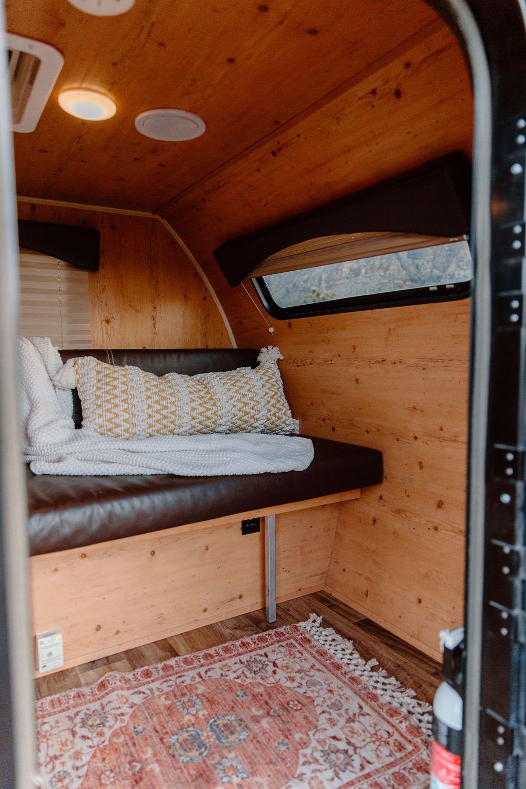 Charming RV rental interior: wooden walls, comfy bench with pillows, a window view, and an inviting rug.. Sunset Park RV SunRay 2018