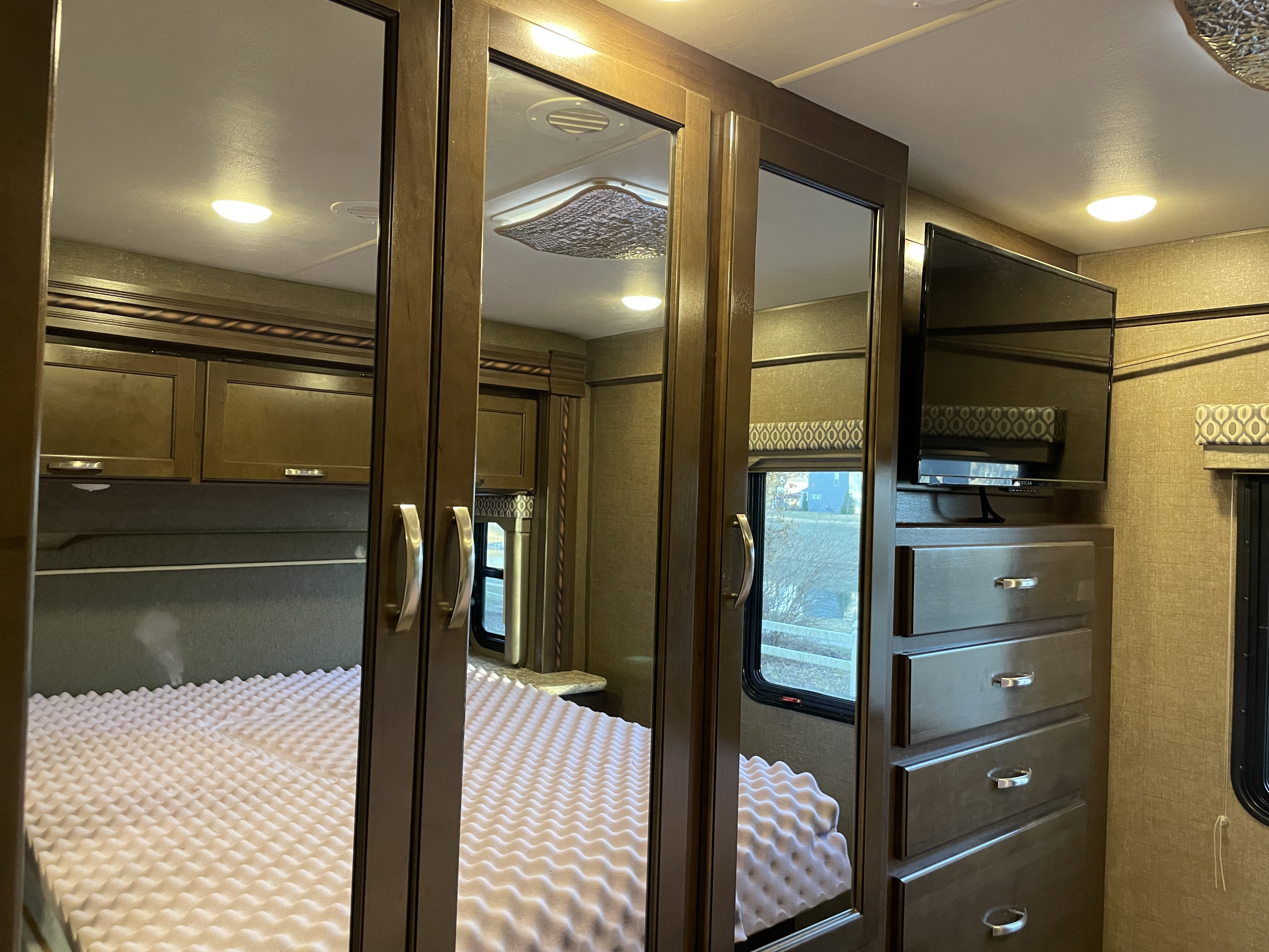 RV rental bedroom with mirrored closet doors reflecting a bed with textured foam. Also visible: a TV, dresser, and overhead cabinets.. Thor Freedom Elite 2017
