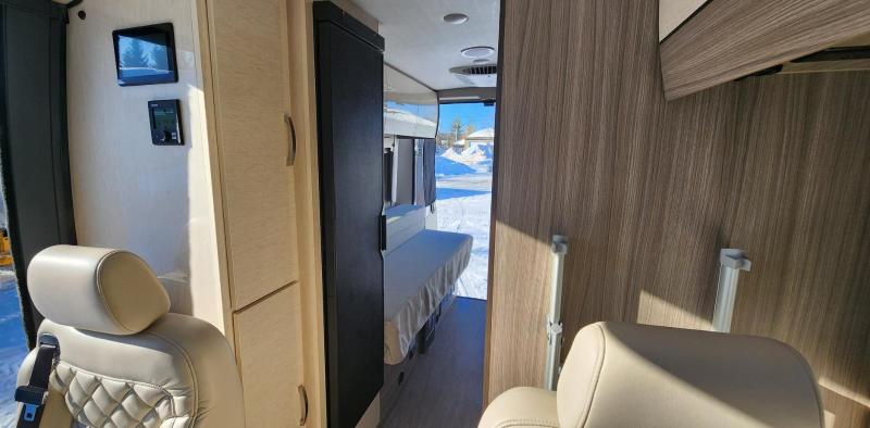 Explore the comfortable interior of this RV rental: quilted seats, digital controls, and a cozy bench with a snowy view.. Entegra Coach Ethos 2023