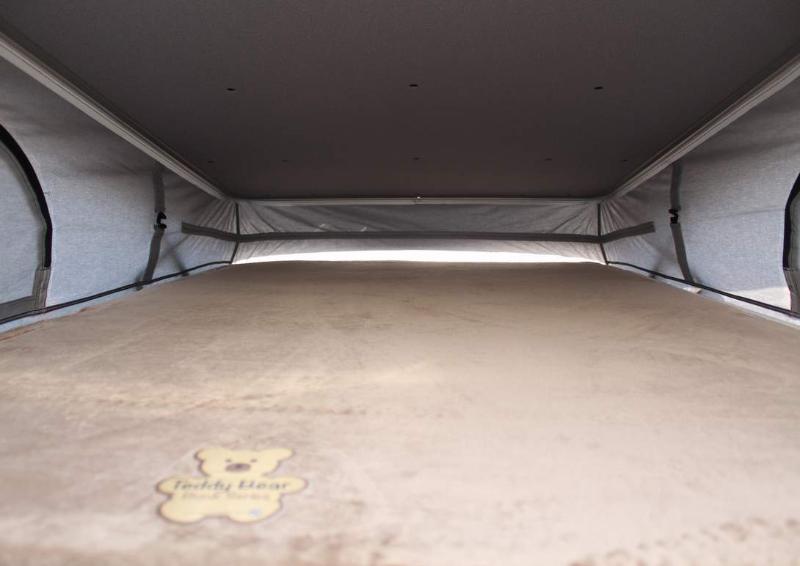 Interior of an RV rental pop-top bed, showing a cozy Teddy Bear blanket within the gray fabric tent walls.. Entegra Coach Ethos 2023