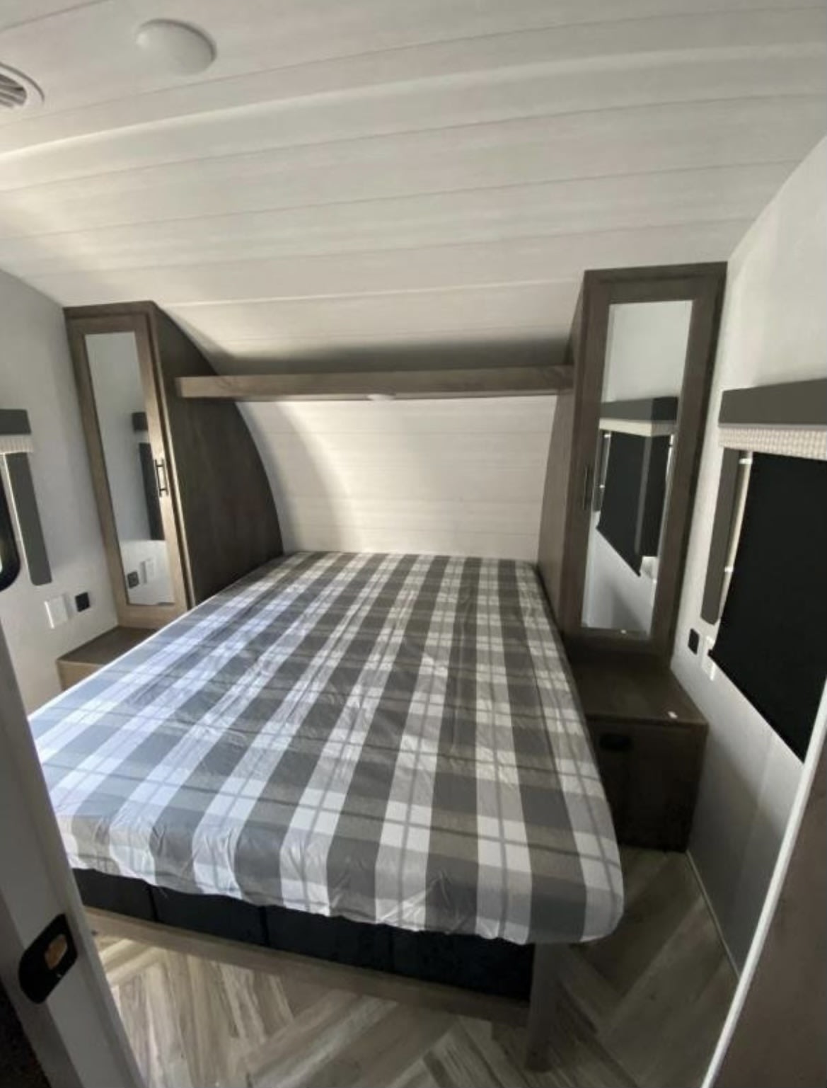 Inside an RV rental, this cozy bedroom features a large plaid bed, mirrored wardrobes, and a practical overhead shelf for comfort.. Forest River Salem Cruise Lite 2021