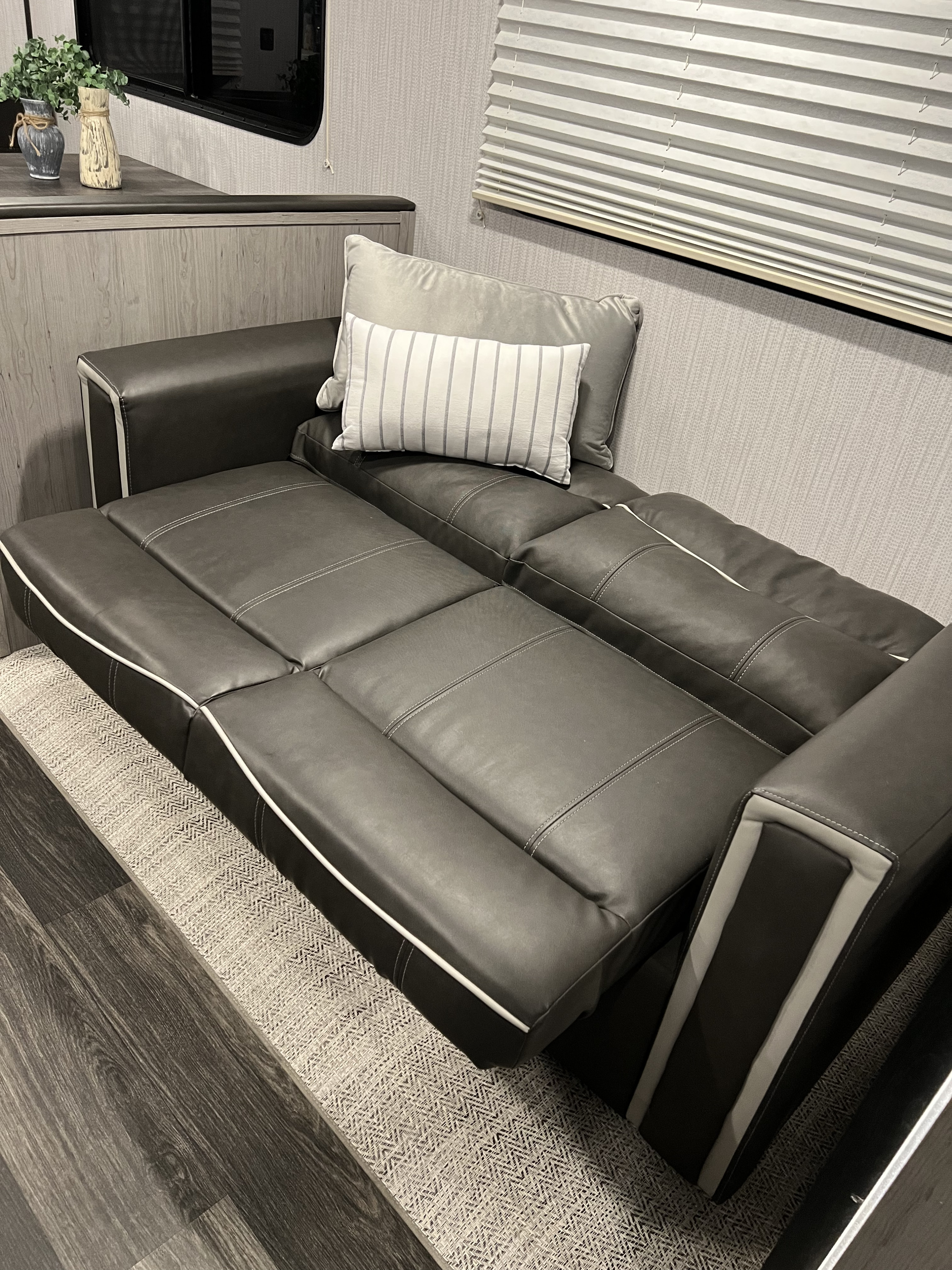 Relax in this modern RV rental's living space: a dark gray convertible sofa bed with striped pillows, counter, and blinds.. Heartland RVs Mallard 2022