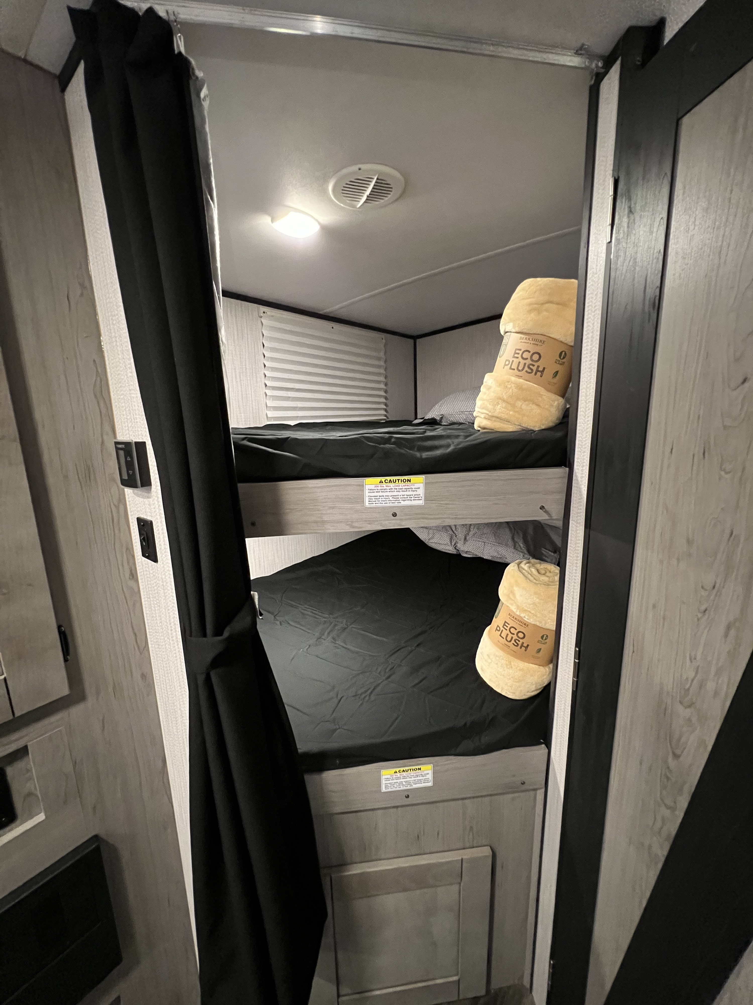 Inside an RV rental, showing cozy bunk beds with black sheets and soft eco-plush blankets. Perfect for family trips.. Heartland RVs Mallard 2022