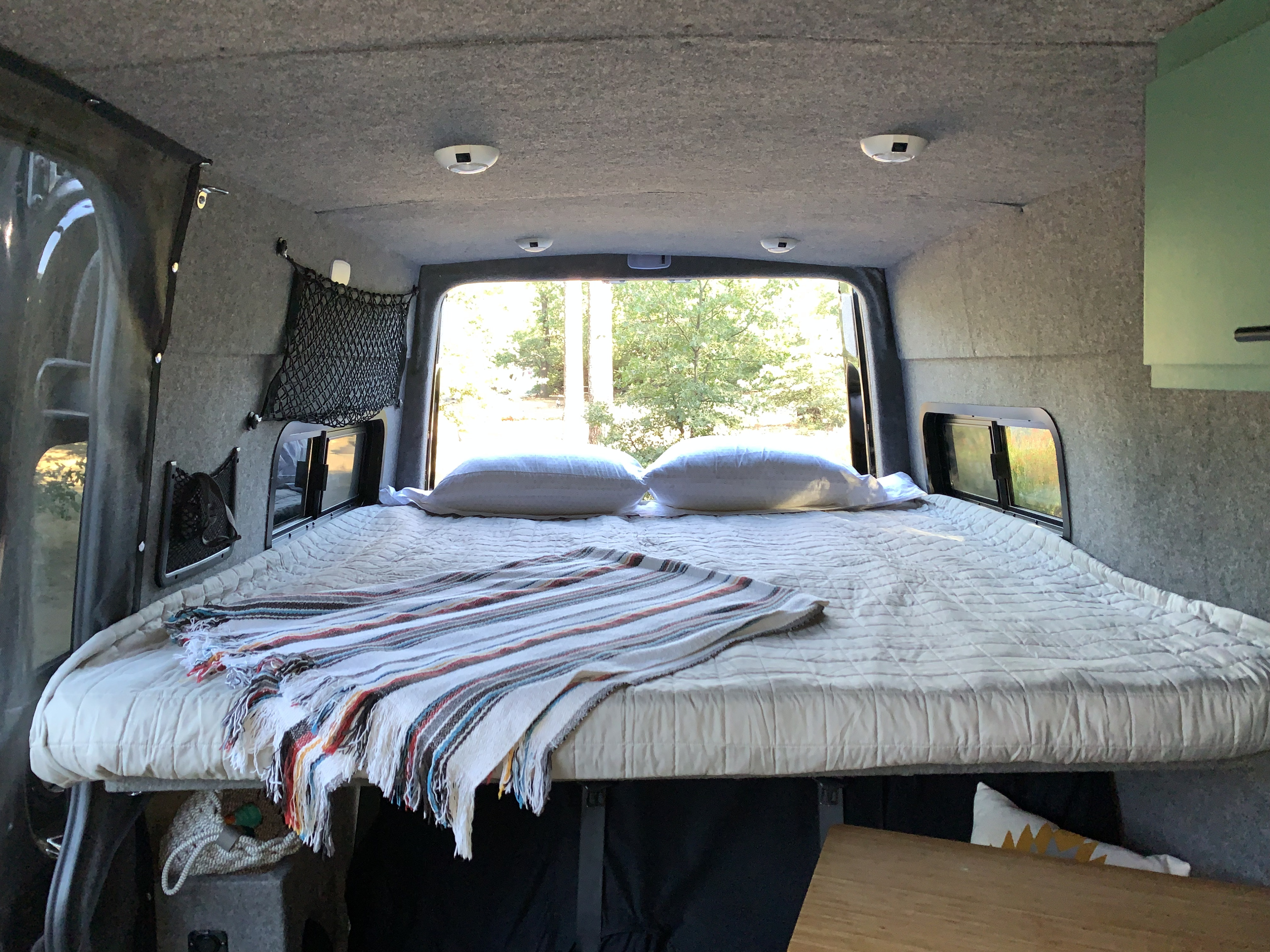 Cozy rv rental camper van interior. Comfortable bed with a quilted cover, ready for rest with peaceful forest views.. Mercedes-Benz Sprinter 2016