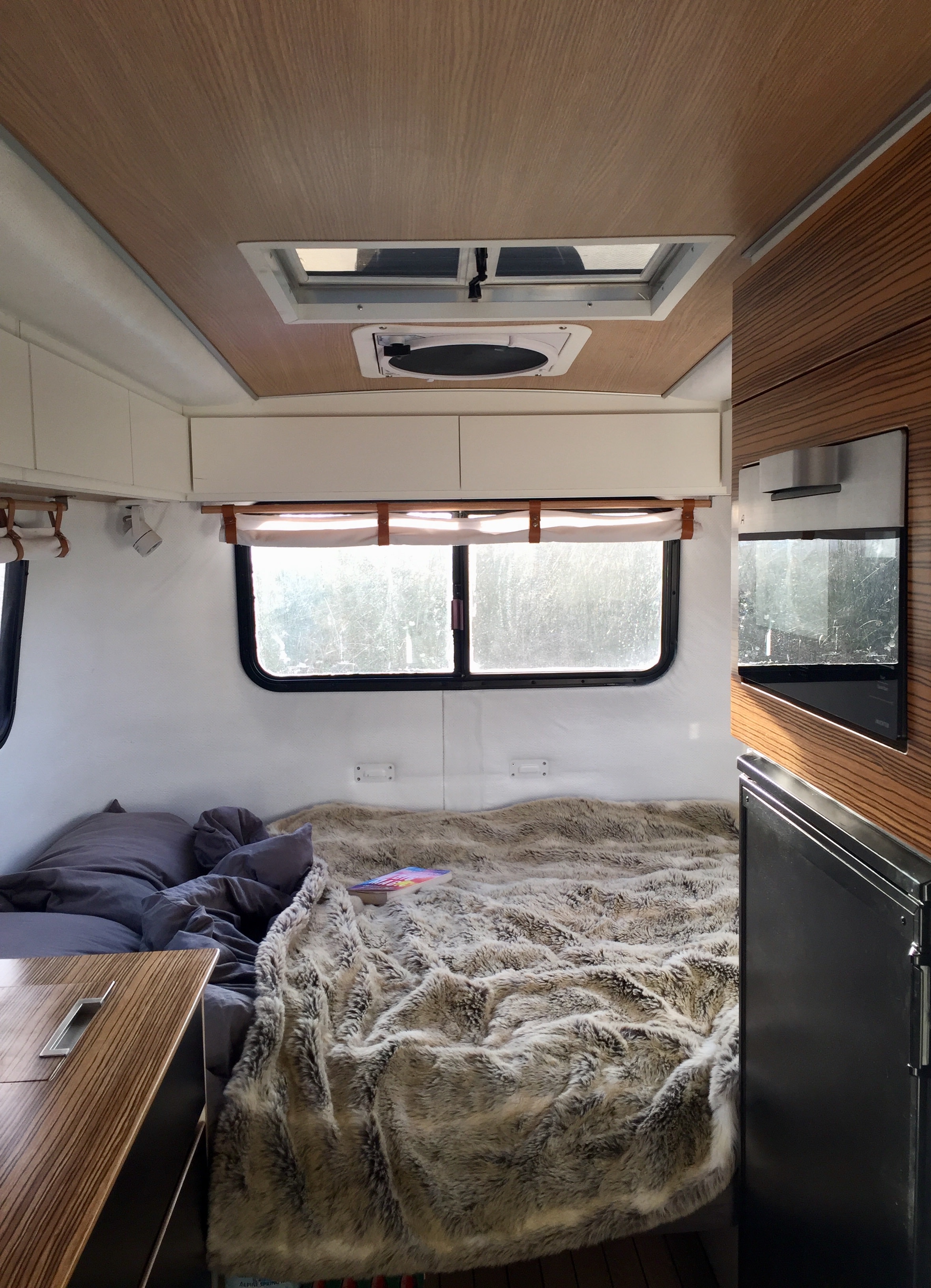 Cozy RV rental interior: Bedroom with plush blanket, bright windows, and compact kitchenette for your next adventure.. Scamp 16' Deluxe 1995