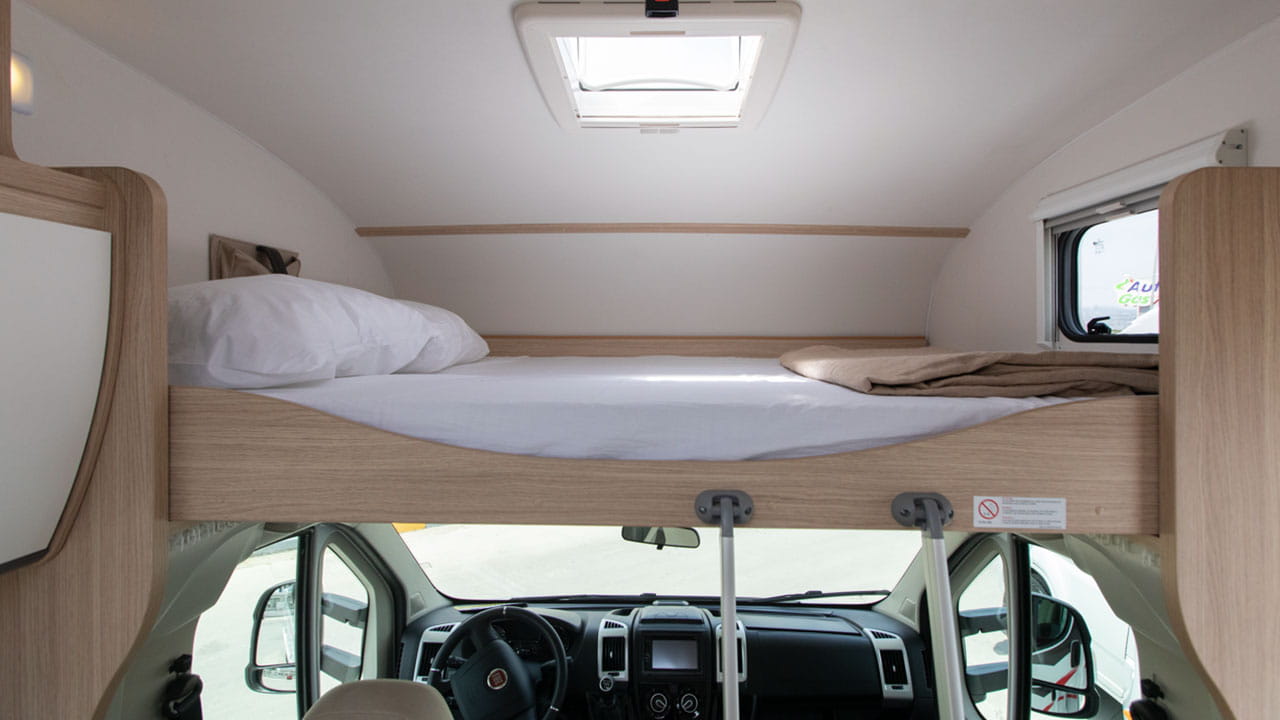 Inside a cozy RV rental: a cab-over bed for sleeping, with the driver's area visible below.. Sunlight A68 2024