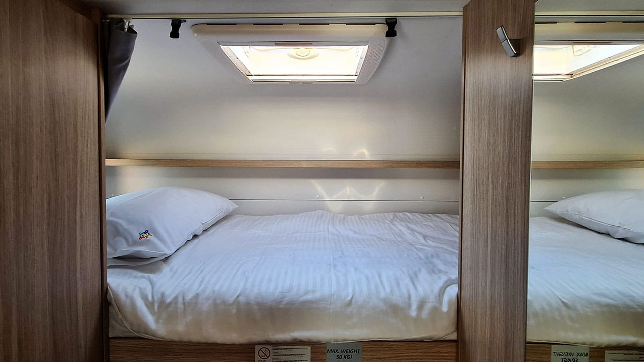 Inside this RV rental, find two tidy bunk beds with white bedding, a ceiling skylight, and a 50kg weight limit for cozy sleeping.. Sunlight A68 2024