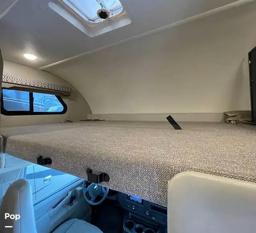 Inside an RV rental: view of the cab-over bunk bed with a window, skylight, and front cockpit below.. Thor Motor Coach Freedom Elite 2020